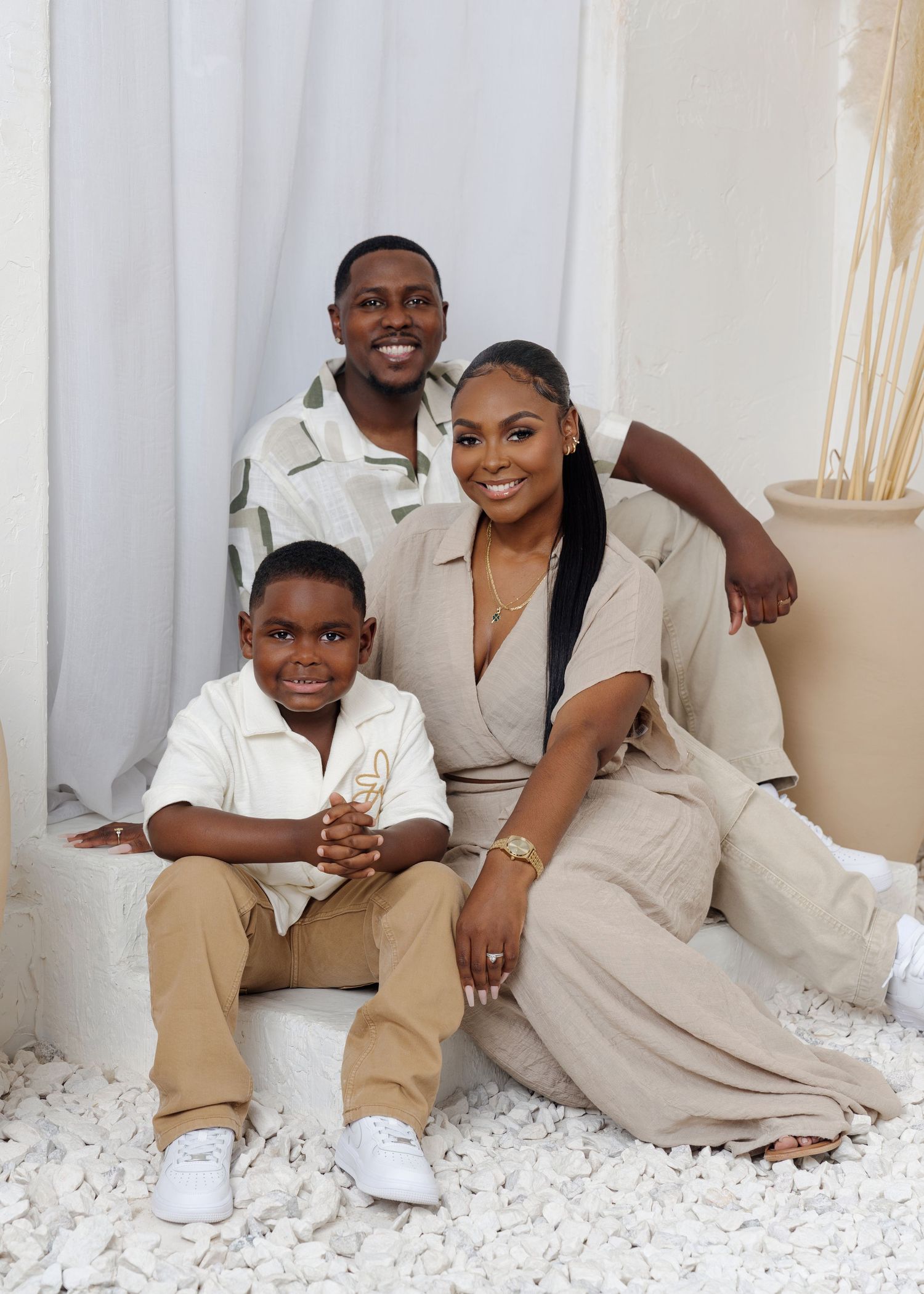 Family in coordinated beige and white outfits posing for portrait on white backdrop.