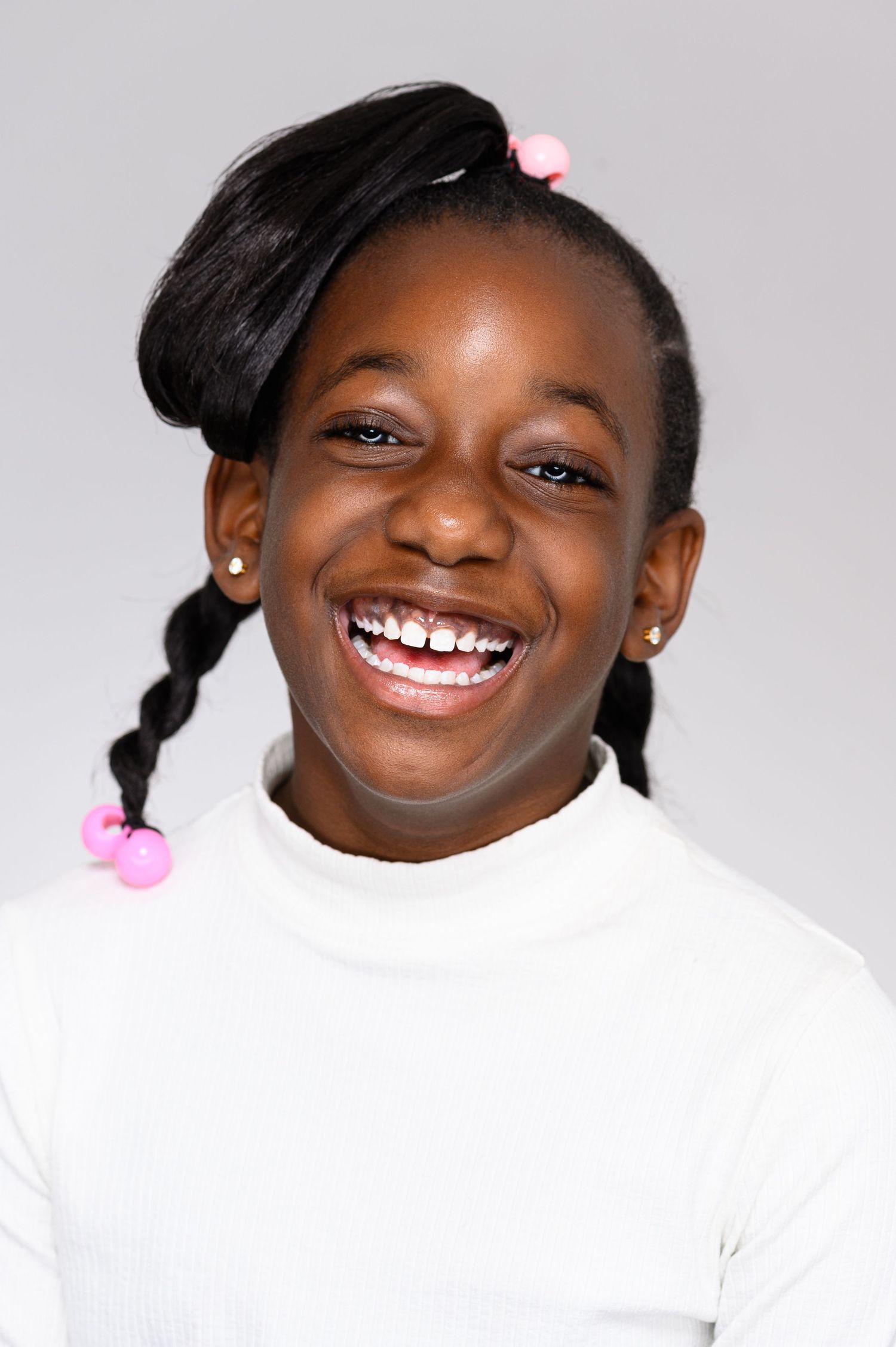 Joyful portraits of a young person in white top with hair accessories smiling brightly.