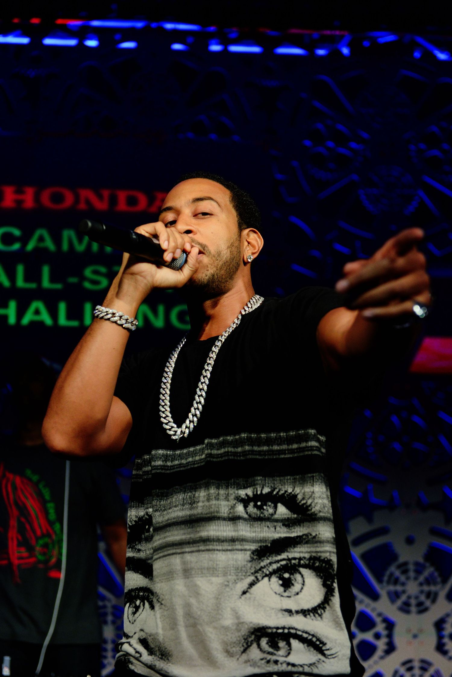 Performer wearing graphic t-shirt with eye design singing on stage with dramatic lighting.