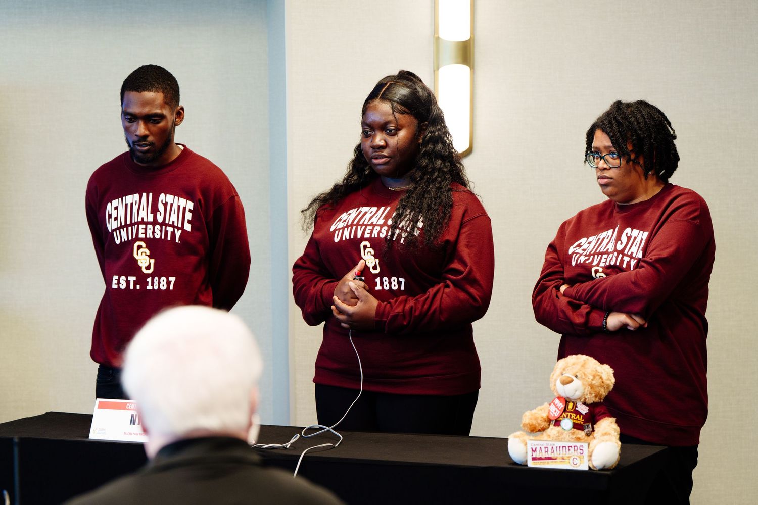 Group wearing matching burgundy sweatshirts seated in an auditorium.