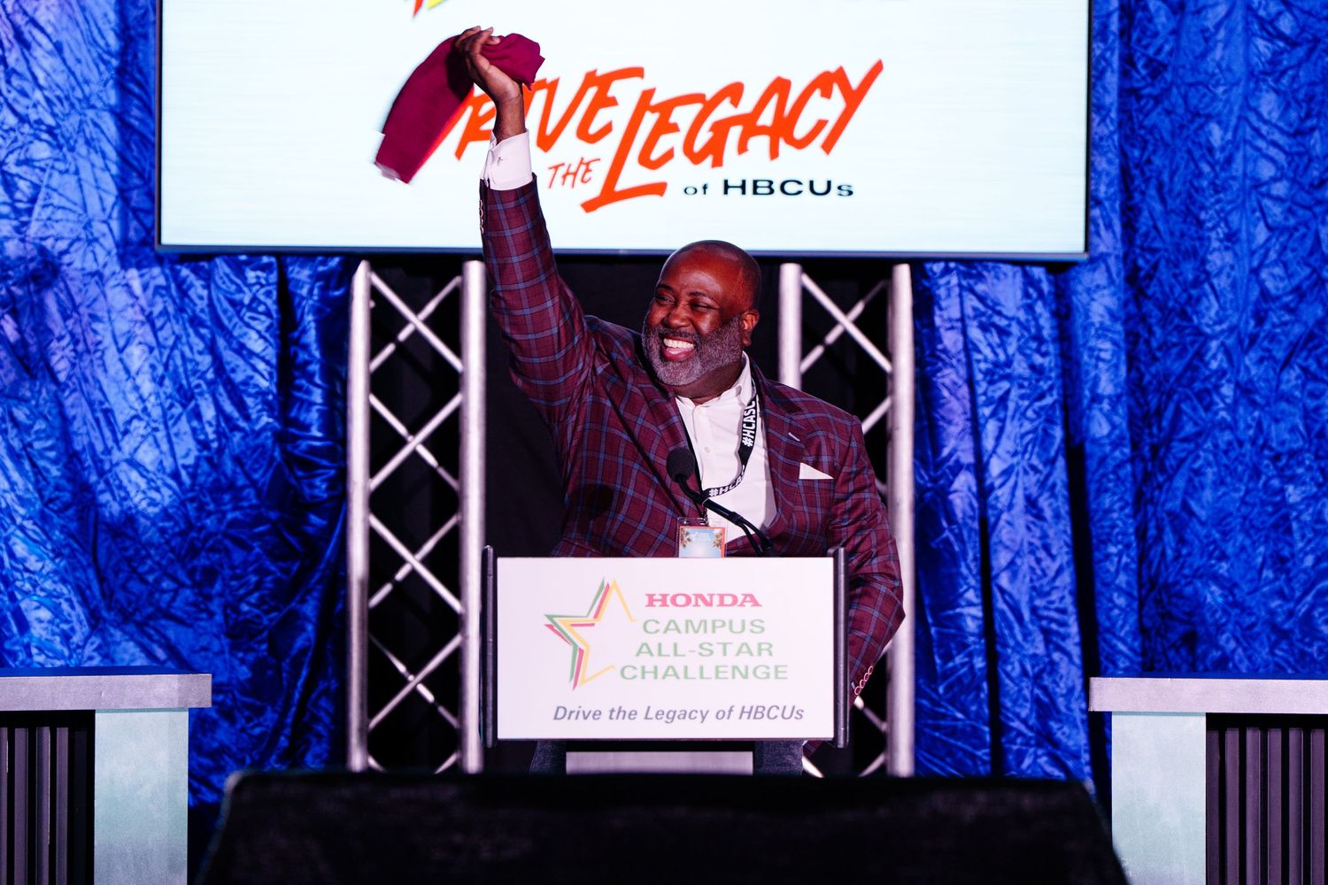 Speaker at a podium during the Live Legacy event with blue stage lighting.