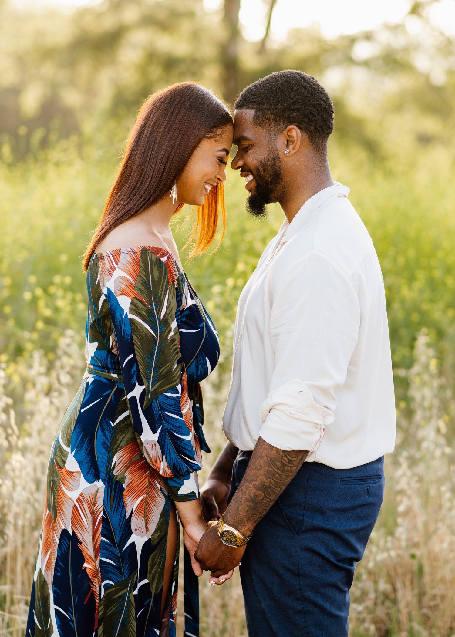 Couple shares an intimate moment in a sunlit meadow wearing coordinated outfits.