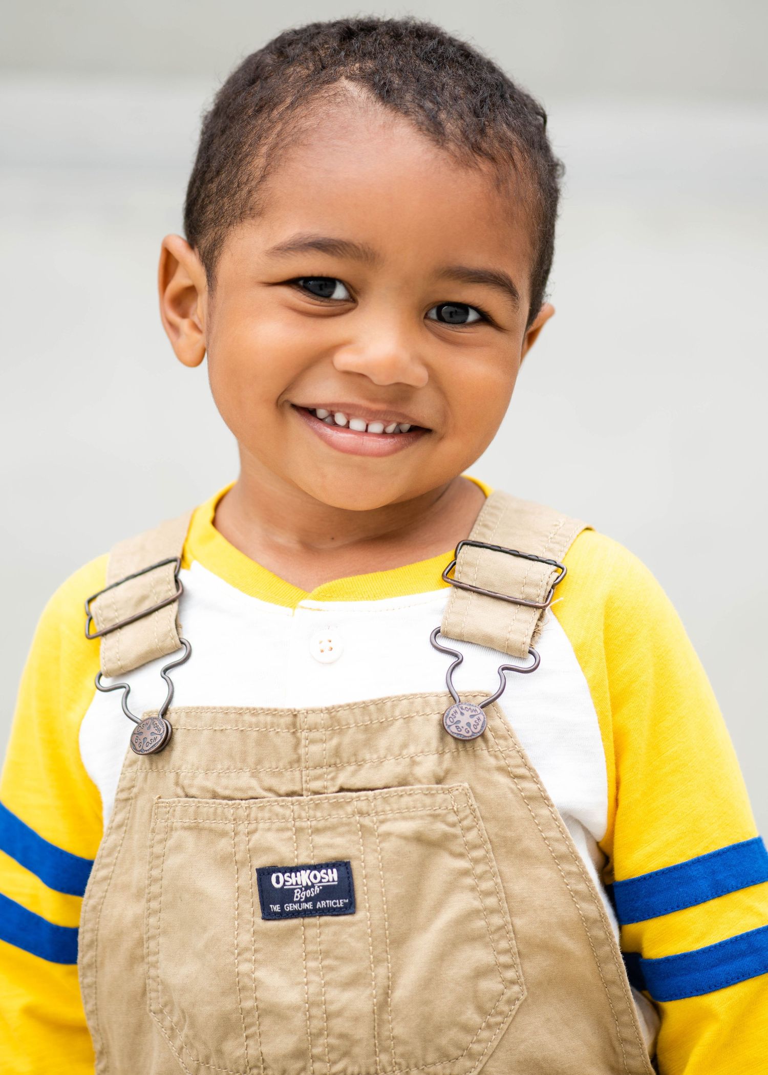 Young child wearing yellow sleeves and tan overalls smiles brightly in a series of progressive shots.