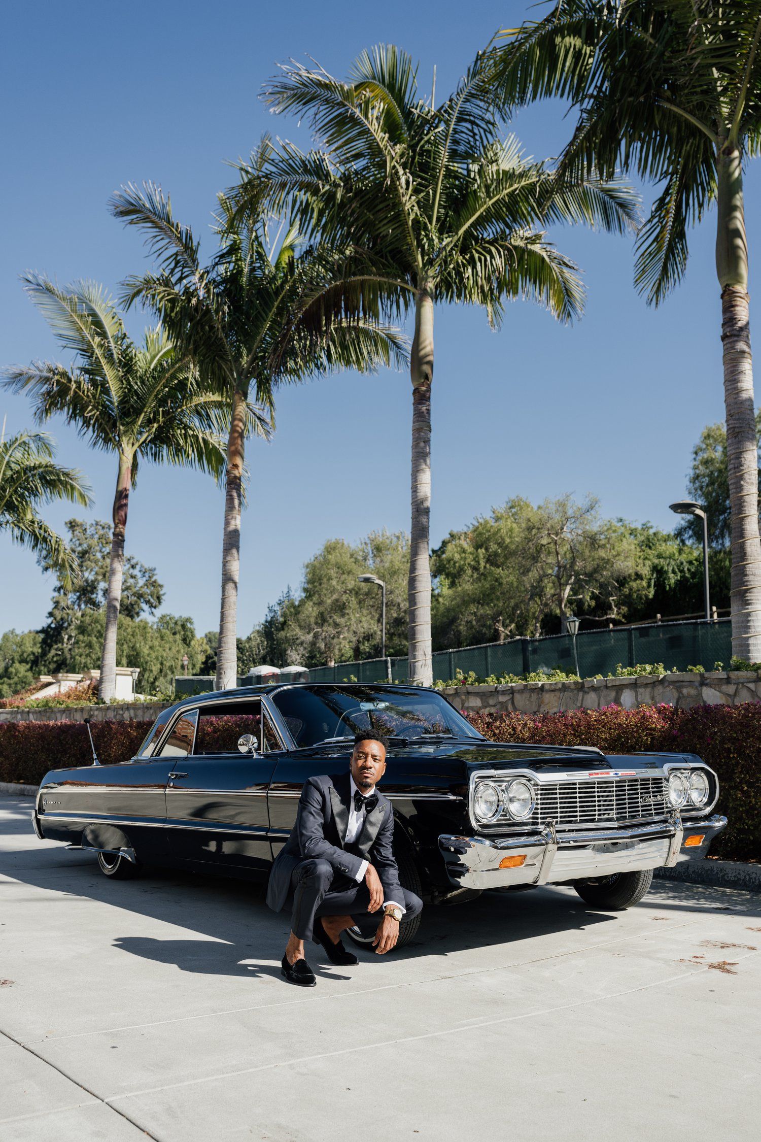 Classic vintage car photoshoot with palm trees and blue sky backdrop.