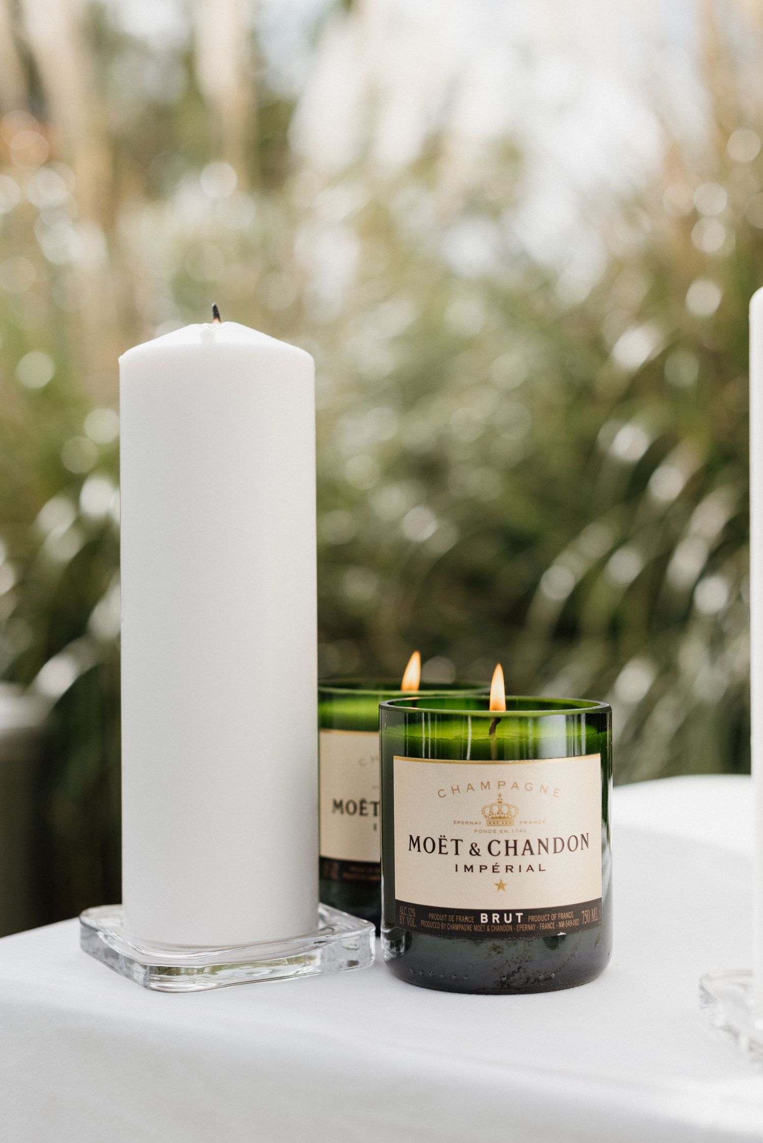 White pillar candle and Moet Chandon champagne bottle candles displayed on white surface.