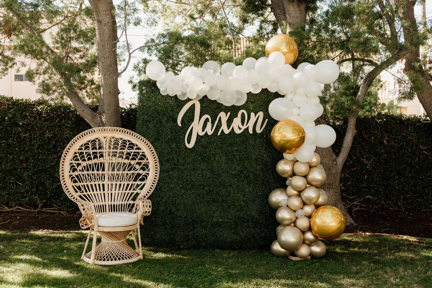 Outdoor party setup with peacock chairs, balloon arches, and garden decorations.