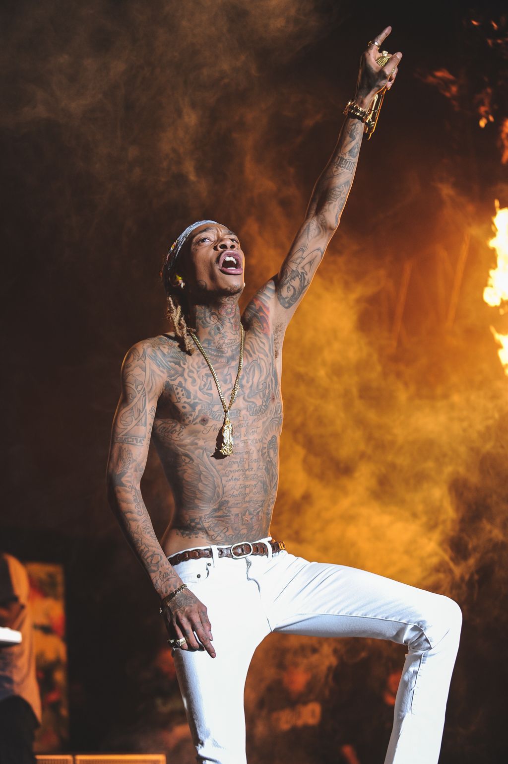 Shirtless performer with tattoos dancing energetically against orange flames on stage.