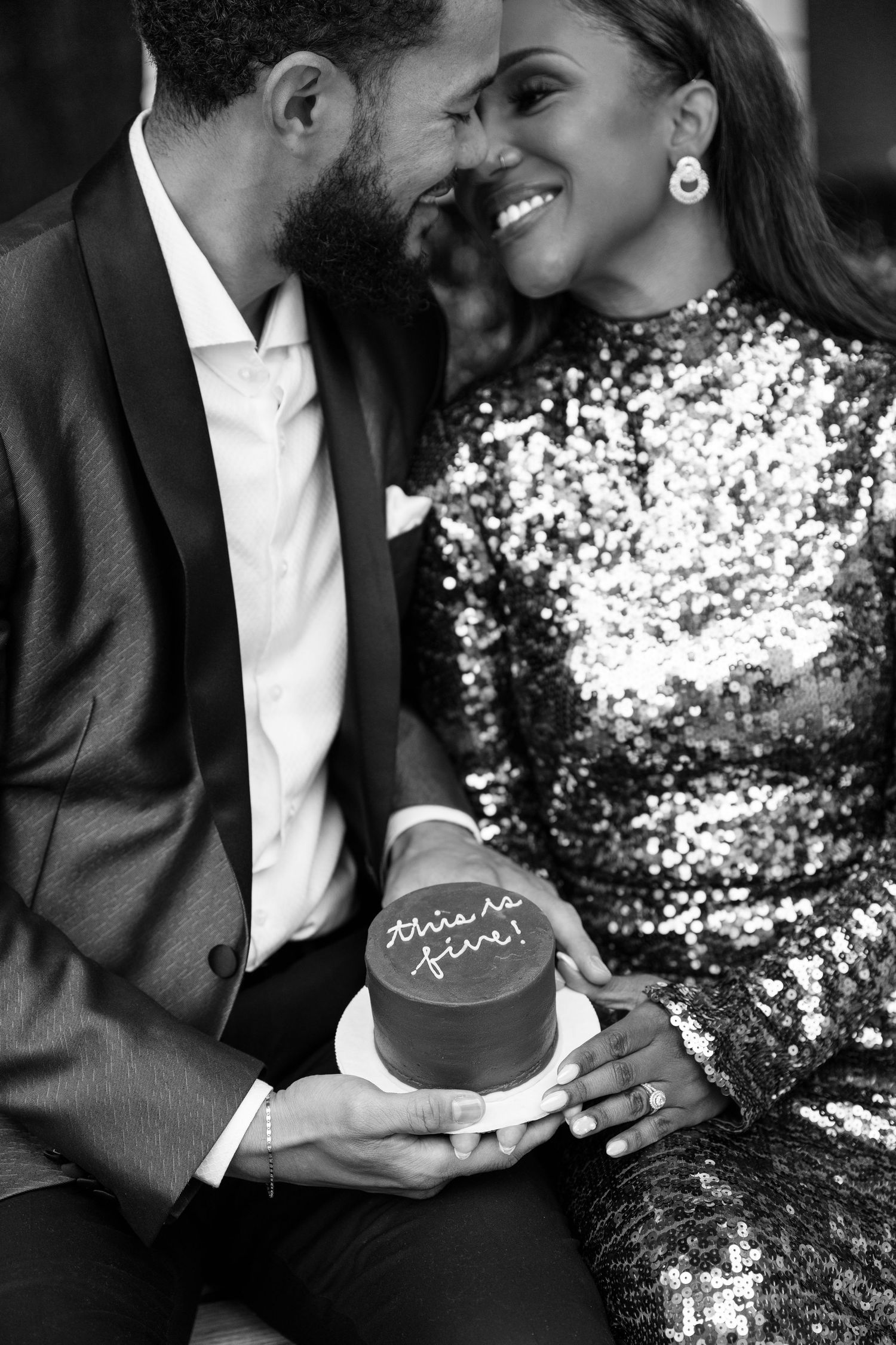 Couple shares intimate moment over dessert in formal attire against sparkly backdrop.