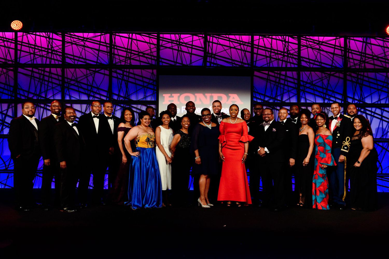 Large group poses on stage with colorful lighting and formal attire.