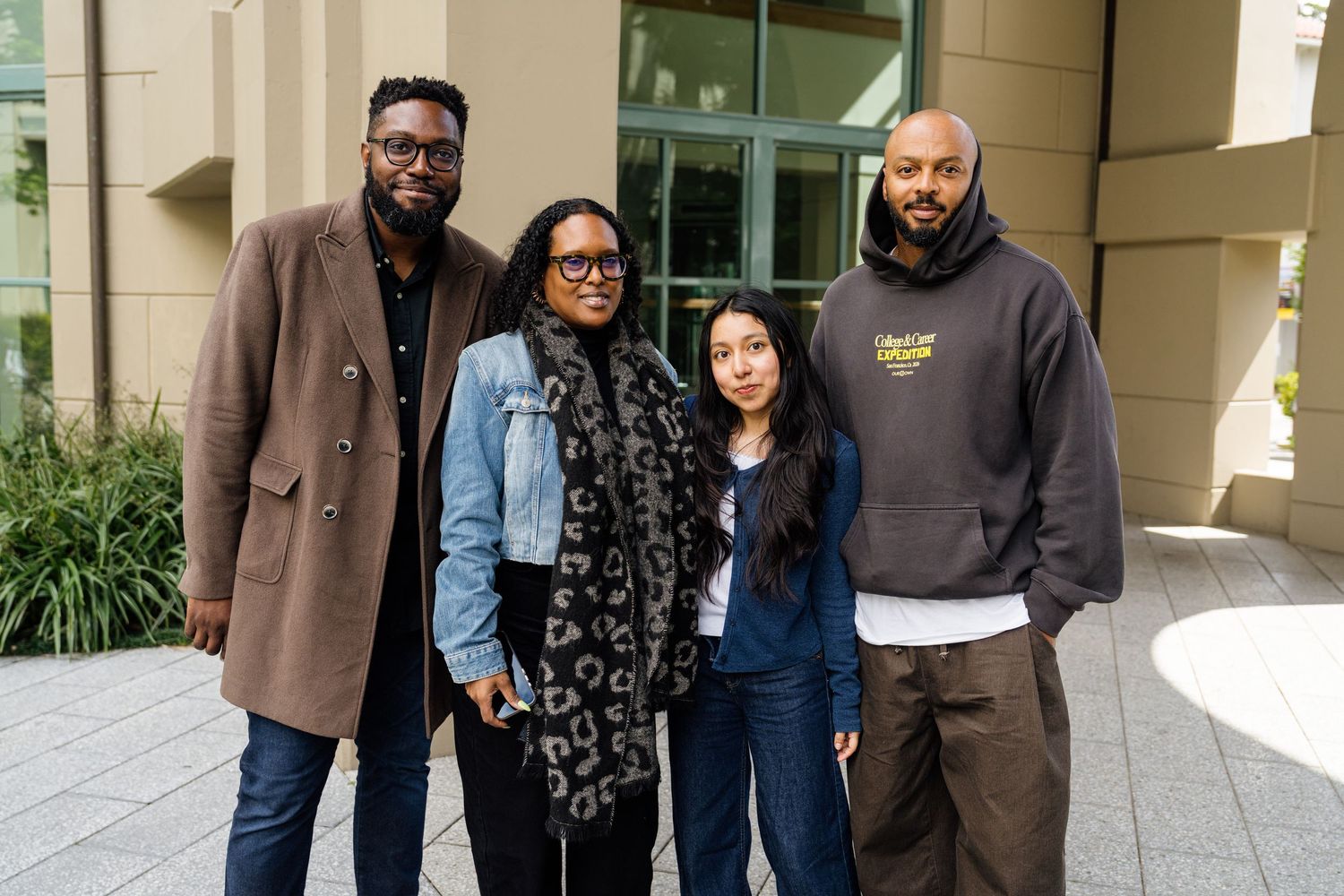 Four people smiling and posing together outdoors near a modern building.