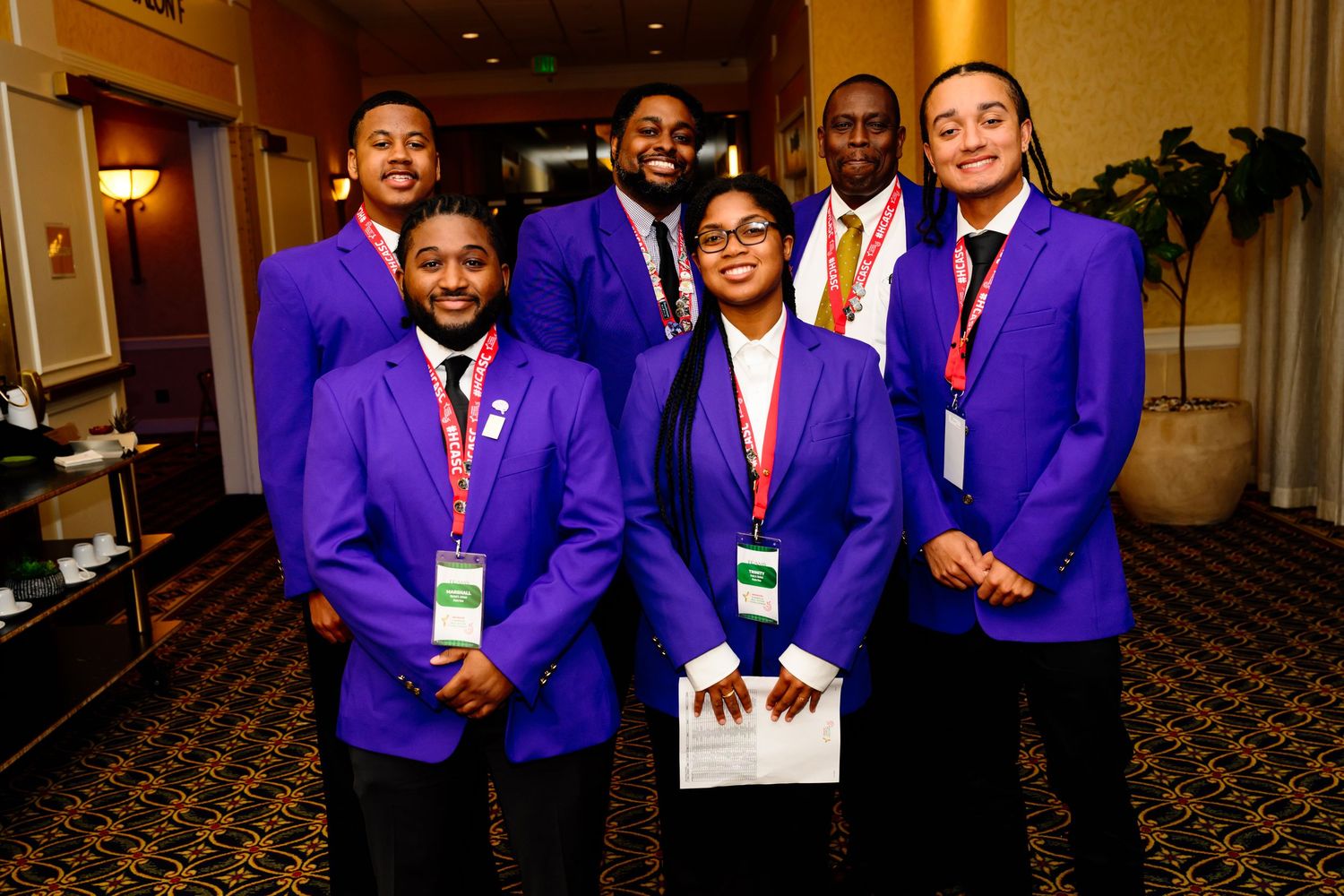 Group wearing matching purple blazers posed together at formal event.