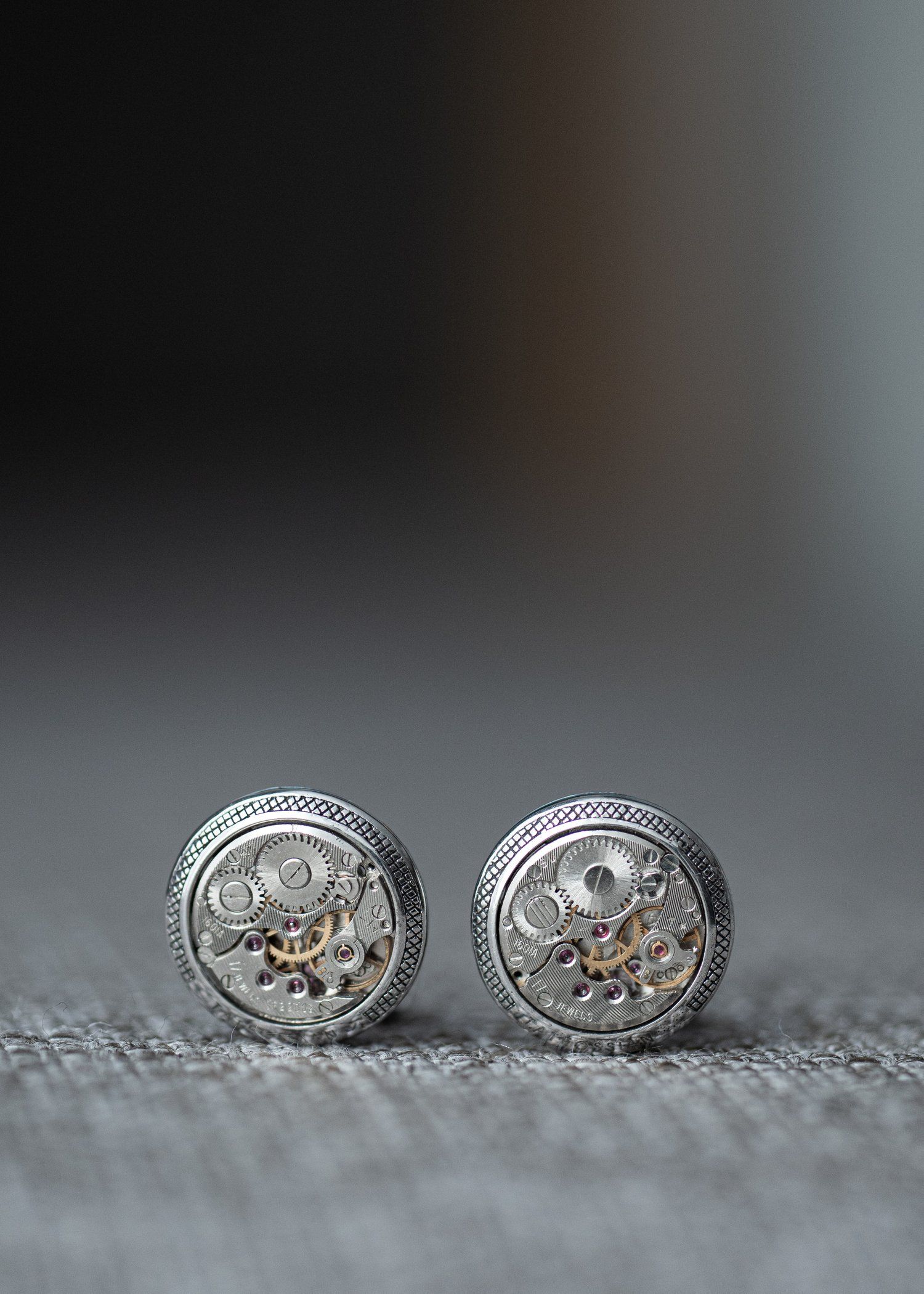 Close-up of vintage-style silver watch movement cufflinks on textured fabric.