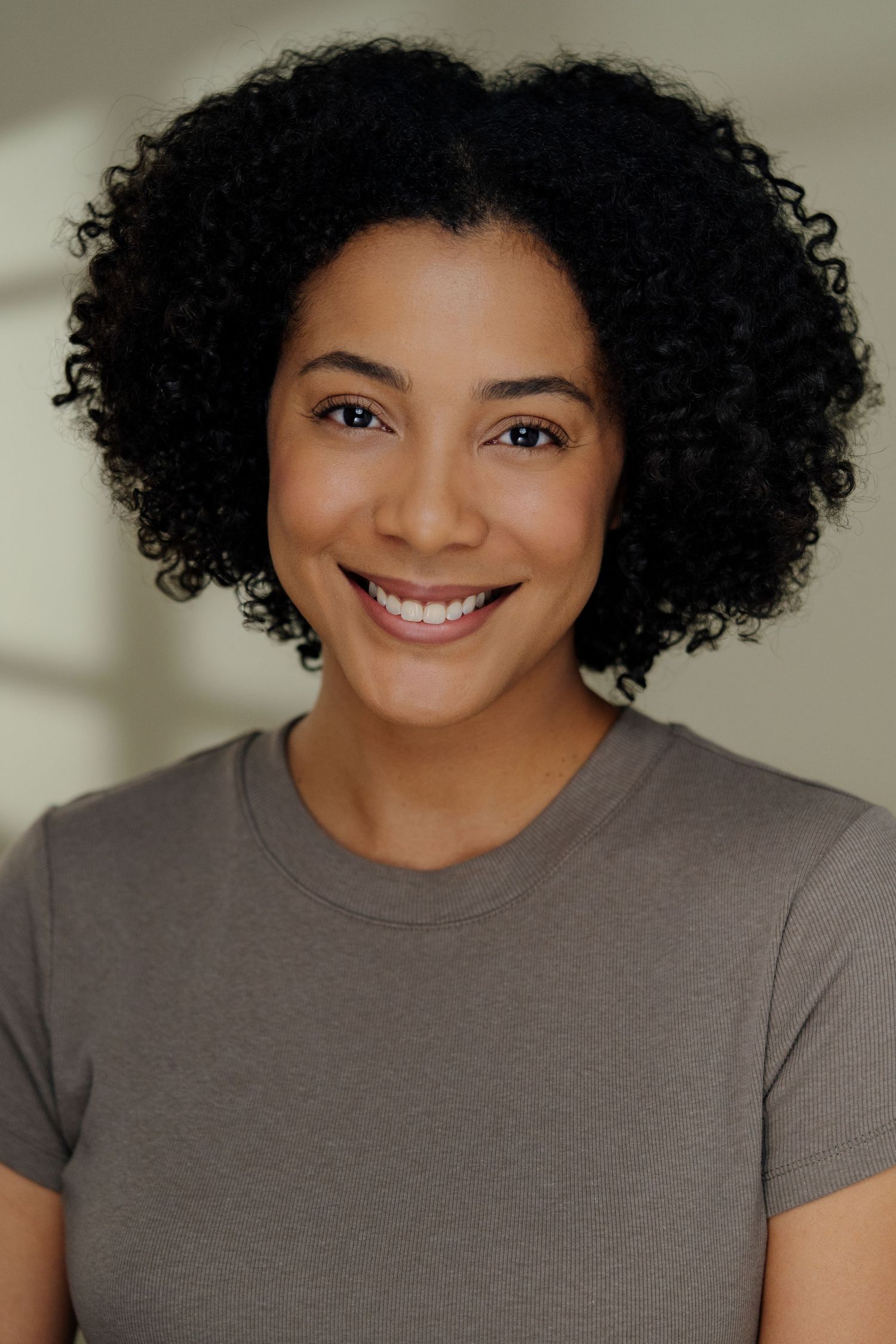 Portrait series showing a person with curly hair and warm smile wearing a grey t-shirt.