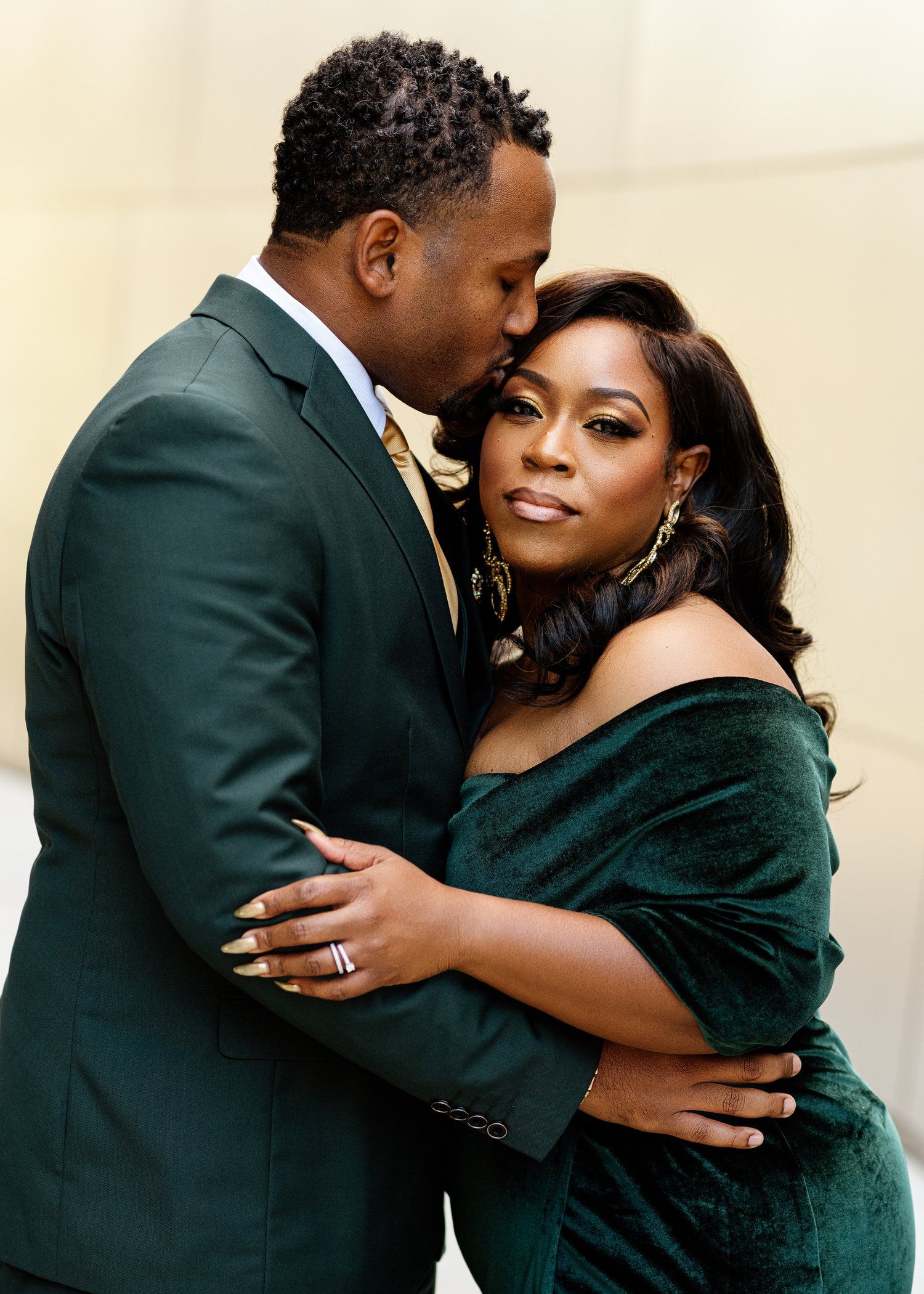 Romantic couple embraces in elegant formal wear with emerald green velvet details.