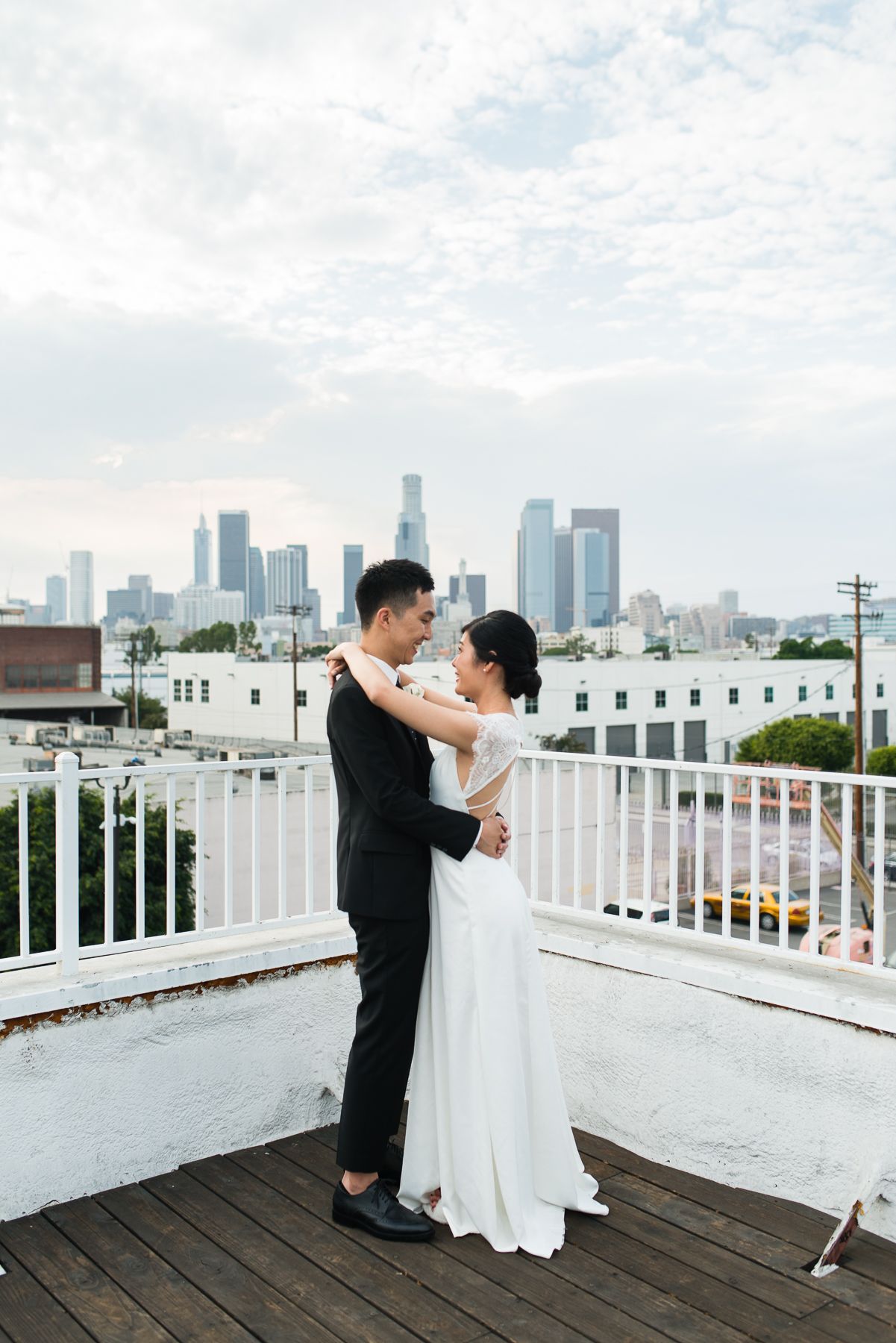 A couple embraces on a rooftop deck with the Los Angeles city skyline visible in the background.
