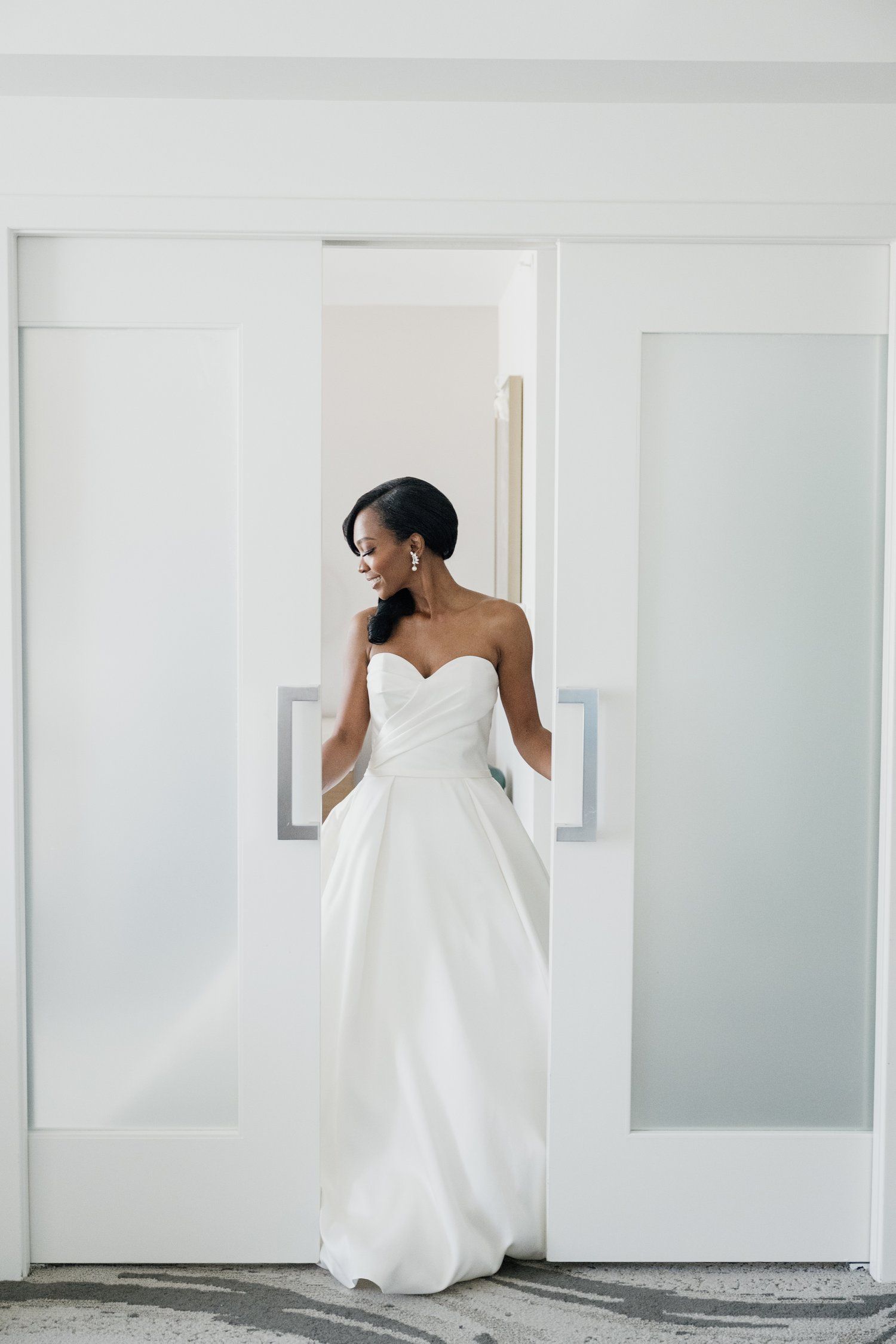 Minimalist bridal portraits in white room showcase flowing wedding gown details.