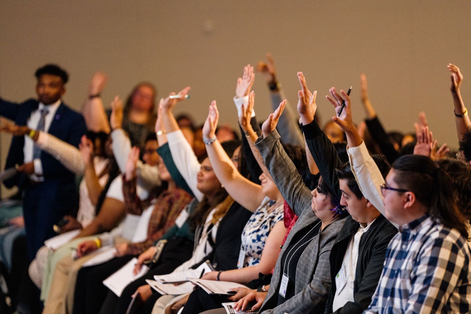 Engaged audience members raising their hands during a presentation or conference.