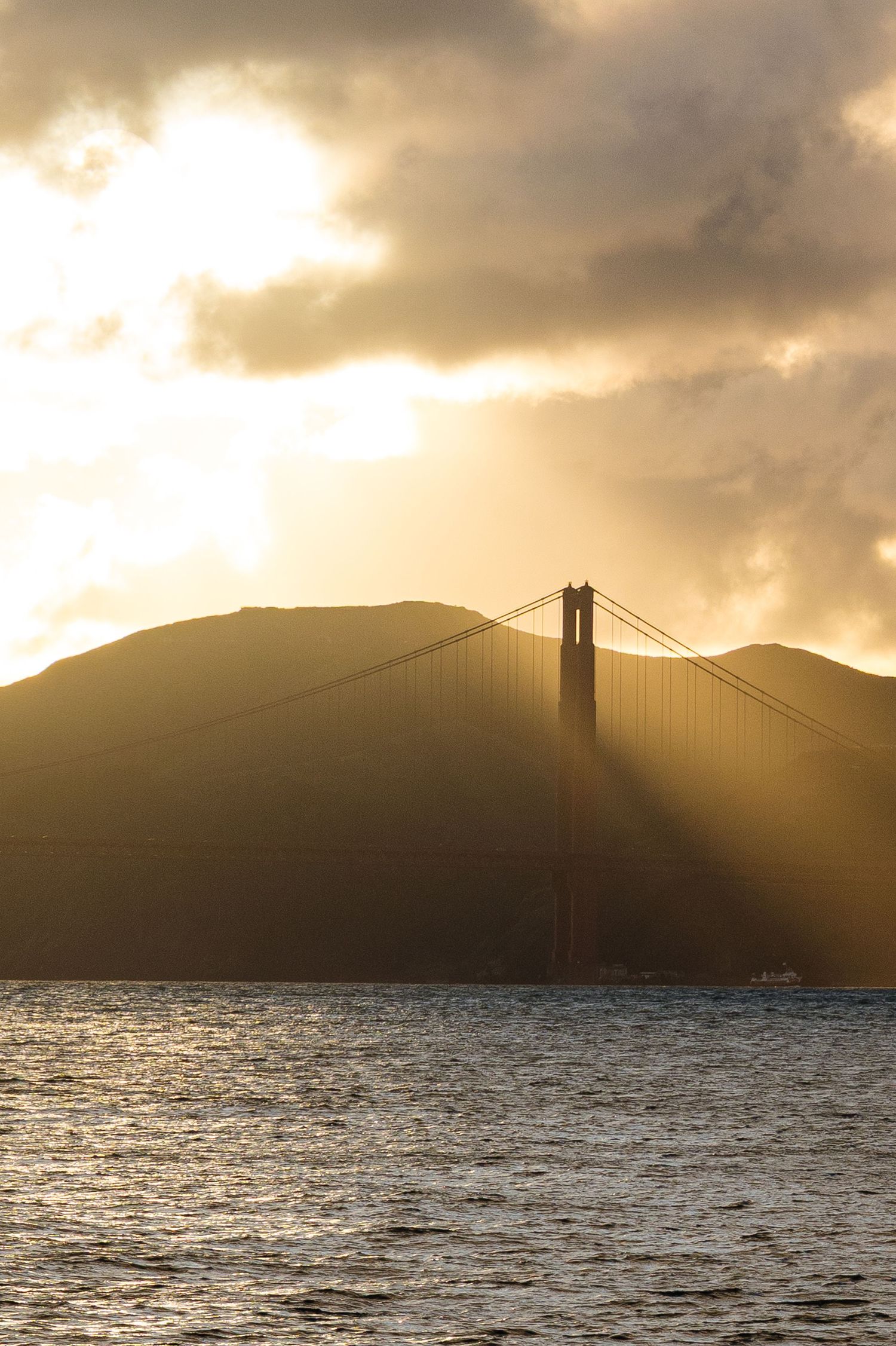 Golden Gate Bridge silhouetted against a dramatic sunset with golden rays breaking through clouds over San Francisco Bay.