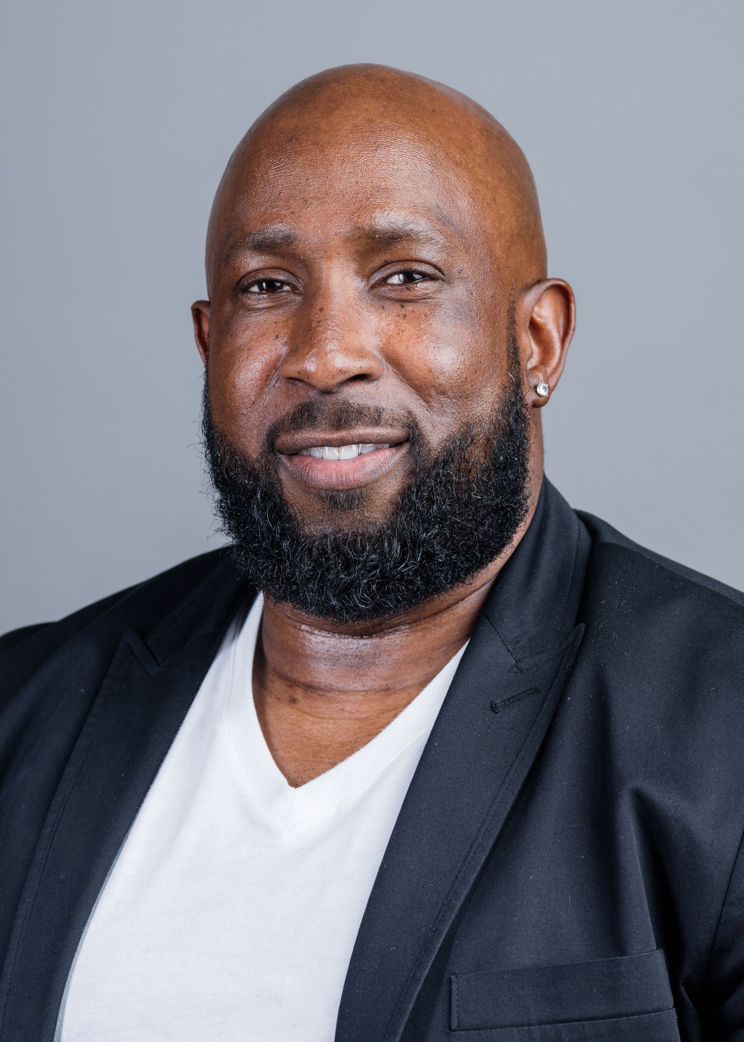 Professional headshot of a smiling person wearing a black blazer and white v-neck shirt.