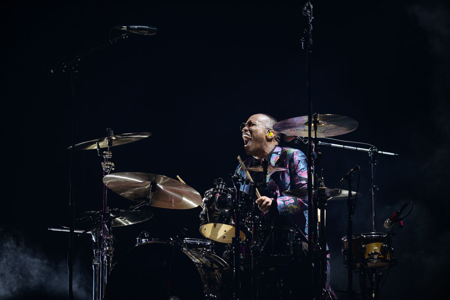 Drummer performing with passion behind drum kit on smoky concert stage.