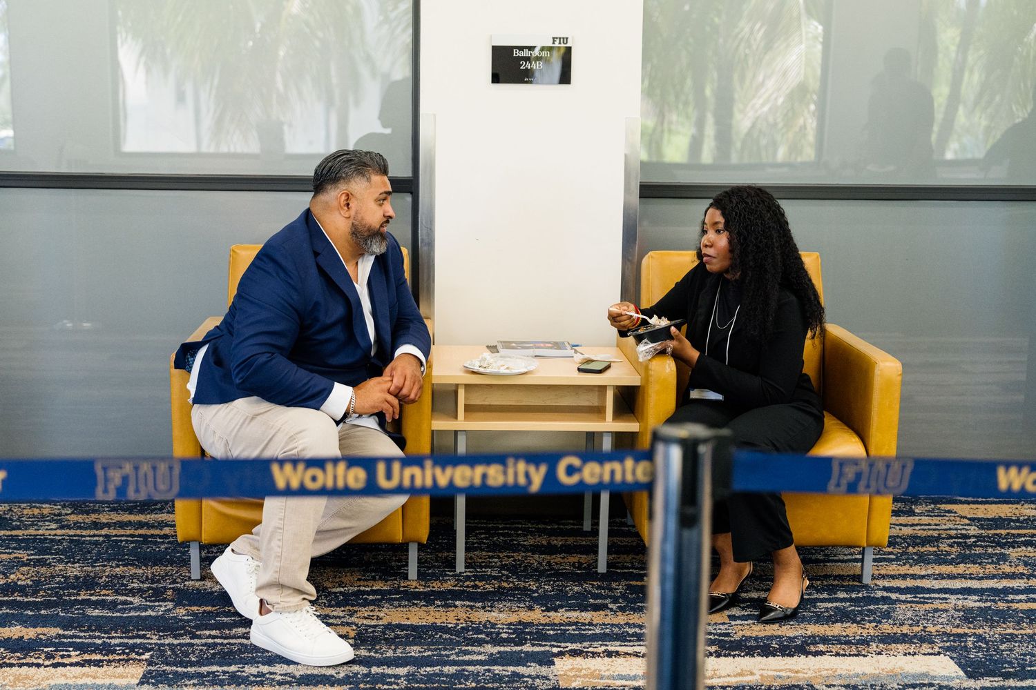Two people having a conversation in yellow chairs at Wolfe University Center.