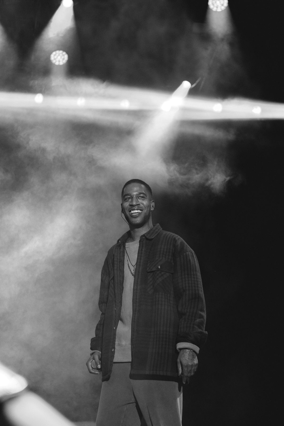 Concert performer in black and white photography with dramatic stage lighting and smoke effects.