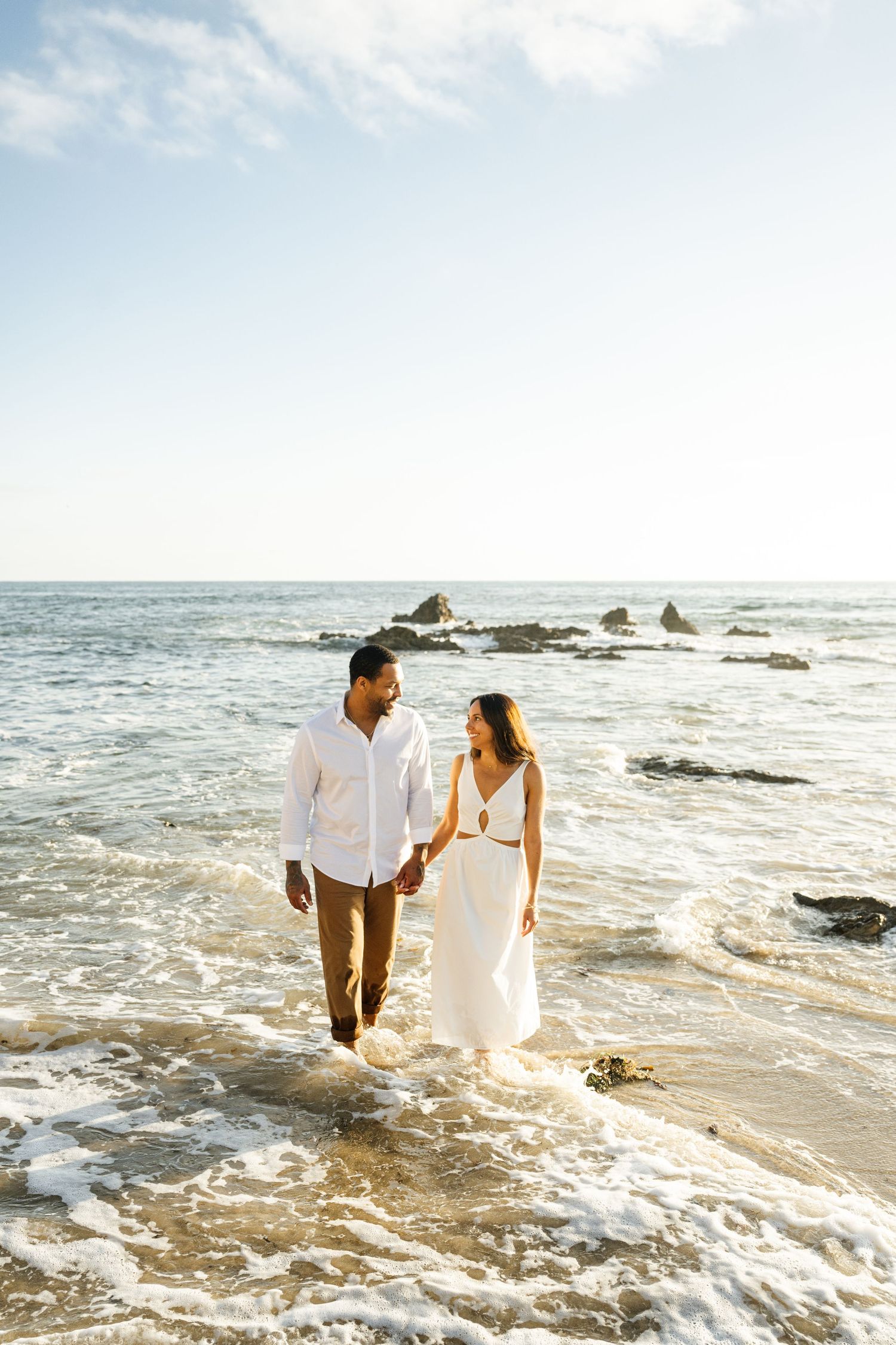 Romantic beach photoshoot with couple playing in ocean waves at sunset.