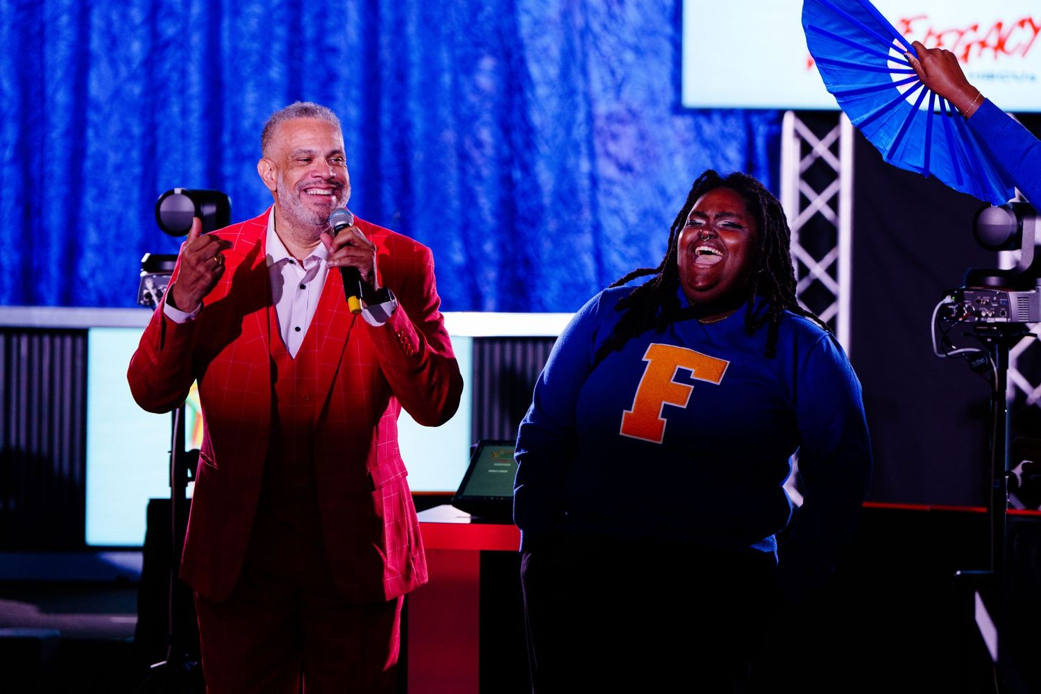 Two performers on stage with blue backdrop during a live event.