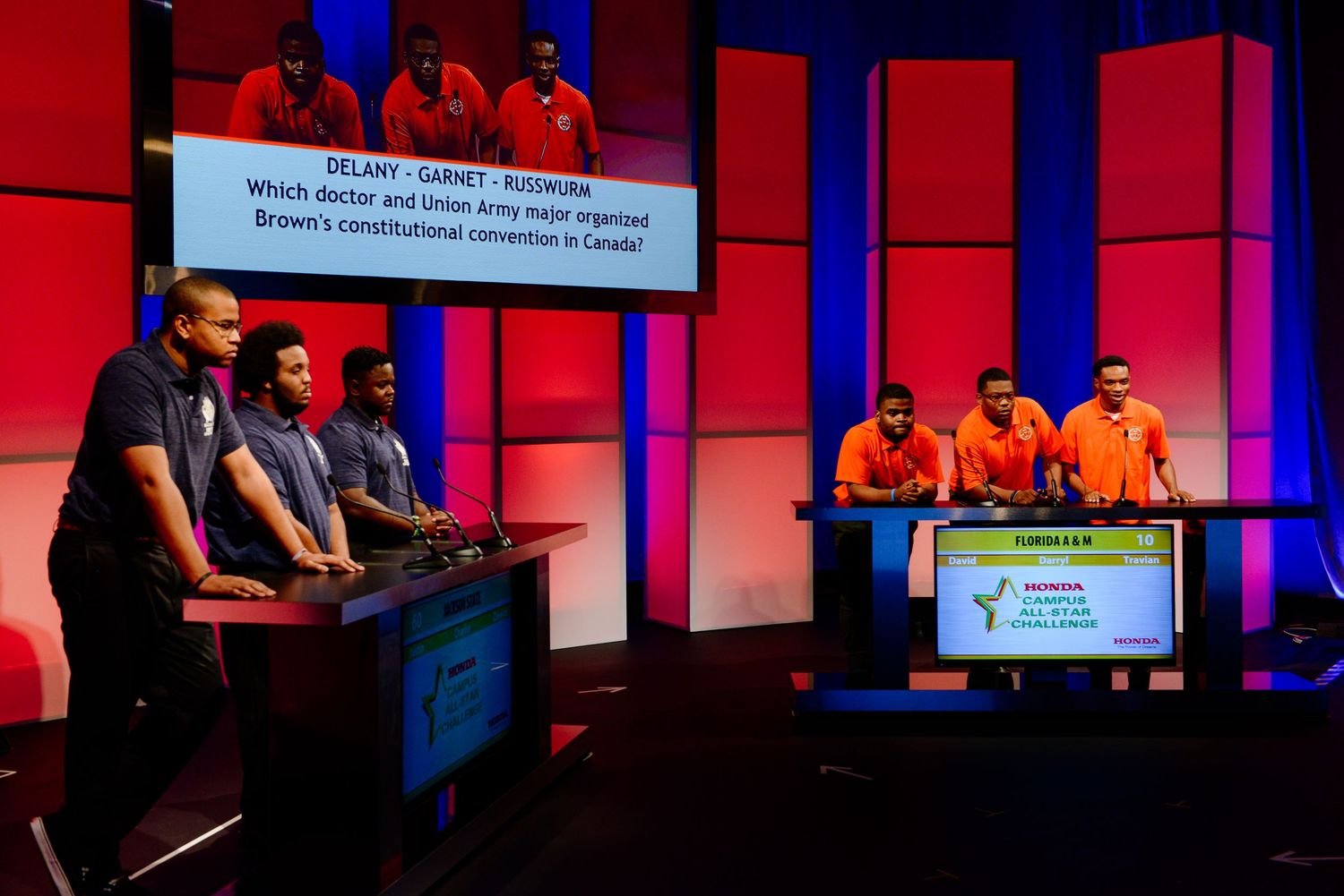 Academic competition stage with red and blue lighting effects and multiple display screens.