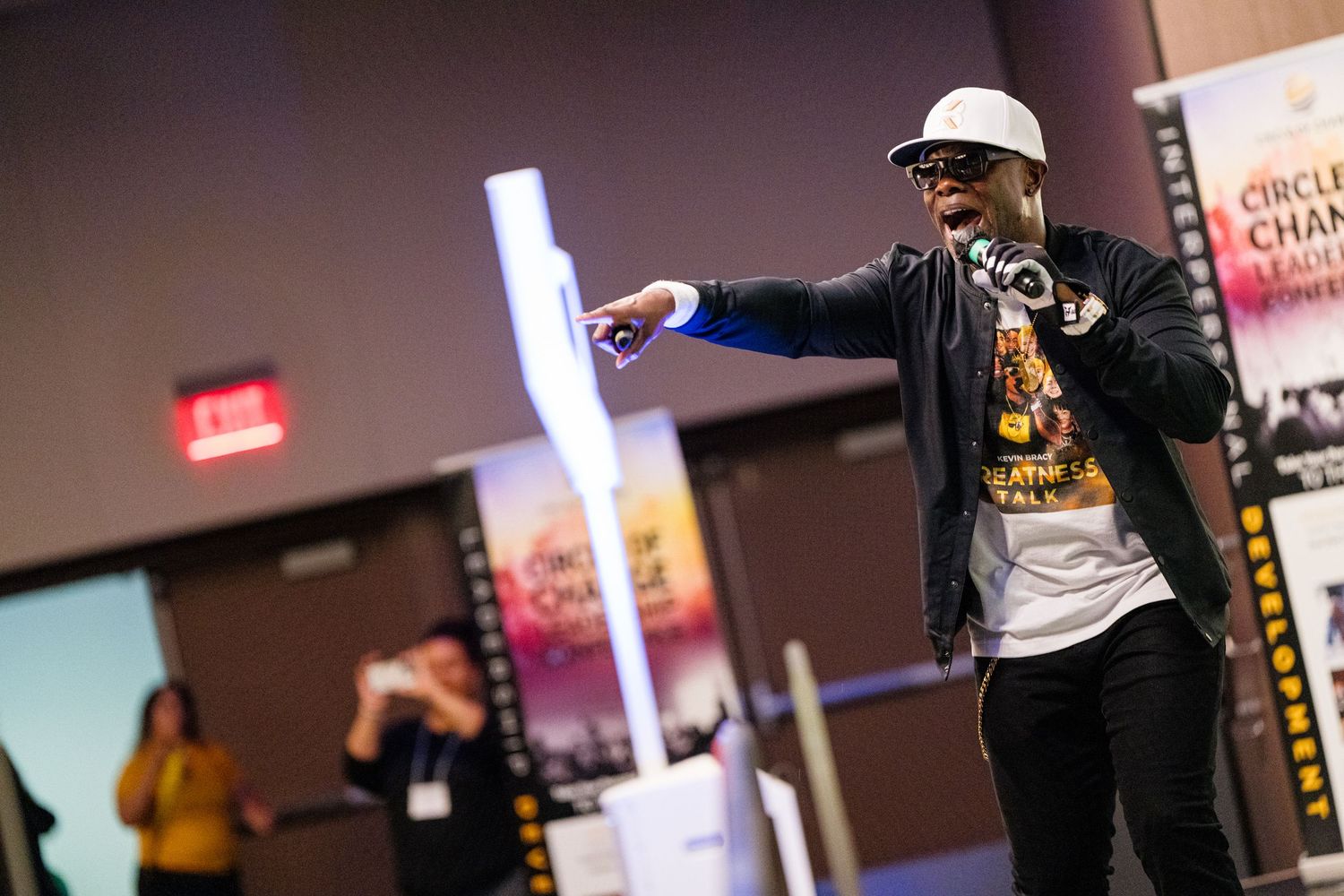 Speaker presenting on stage at a leadership conference with branded backdrop.
