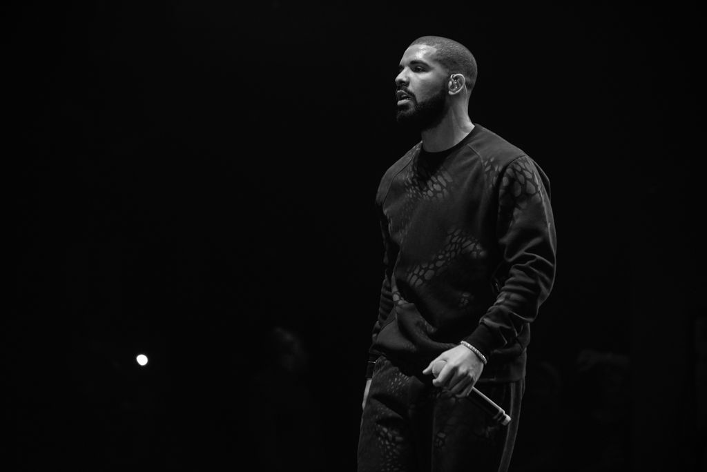 Performer in dark clothing stands on dimly lit stage during dramatic concert performance.