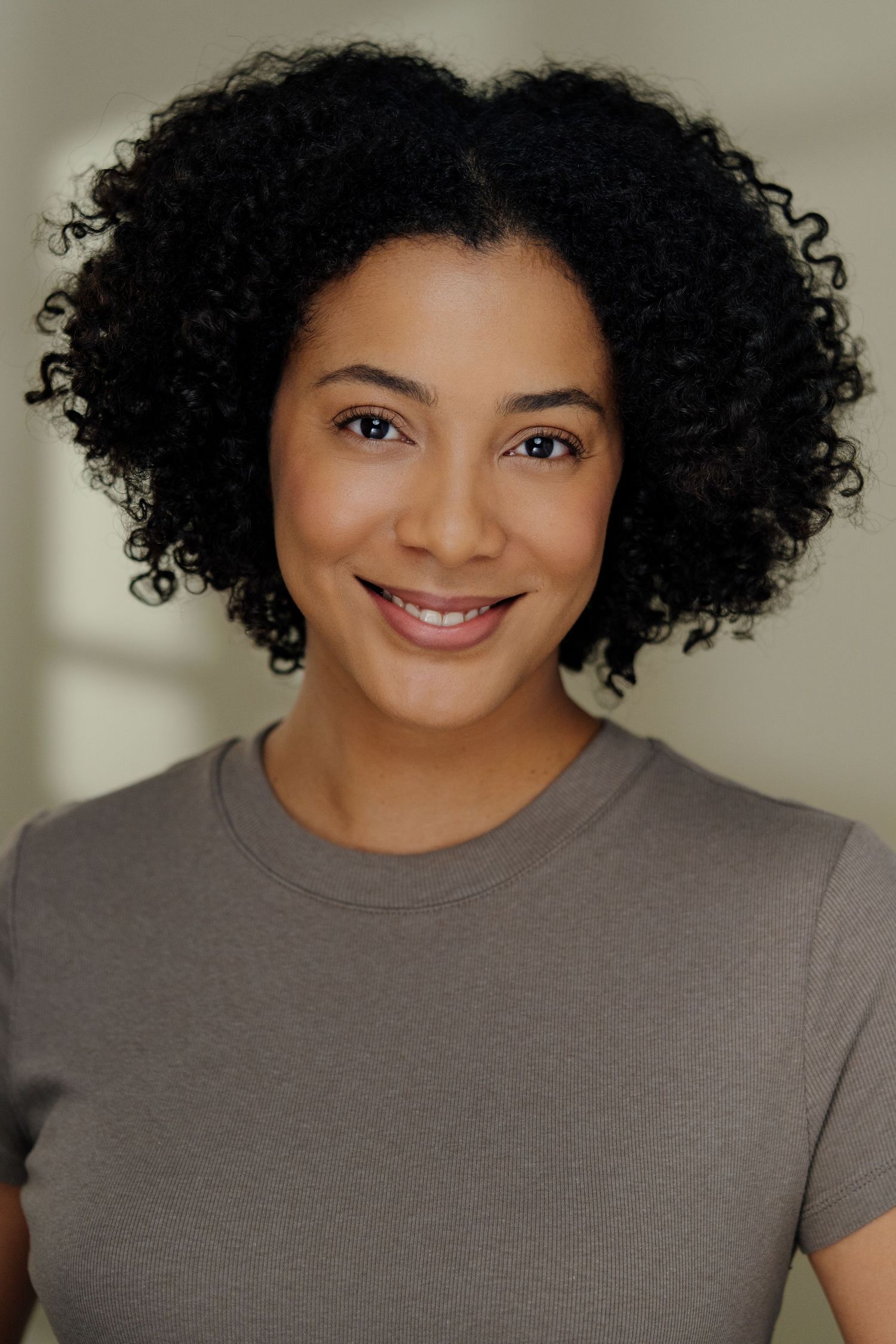 Portrait of person with natural curly hair wearing grey t-shirt against neutral background.