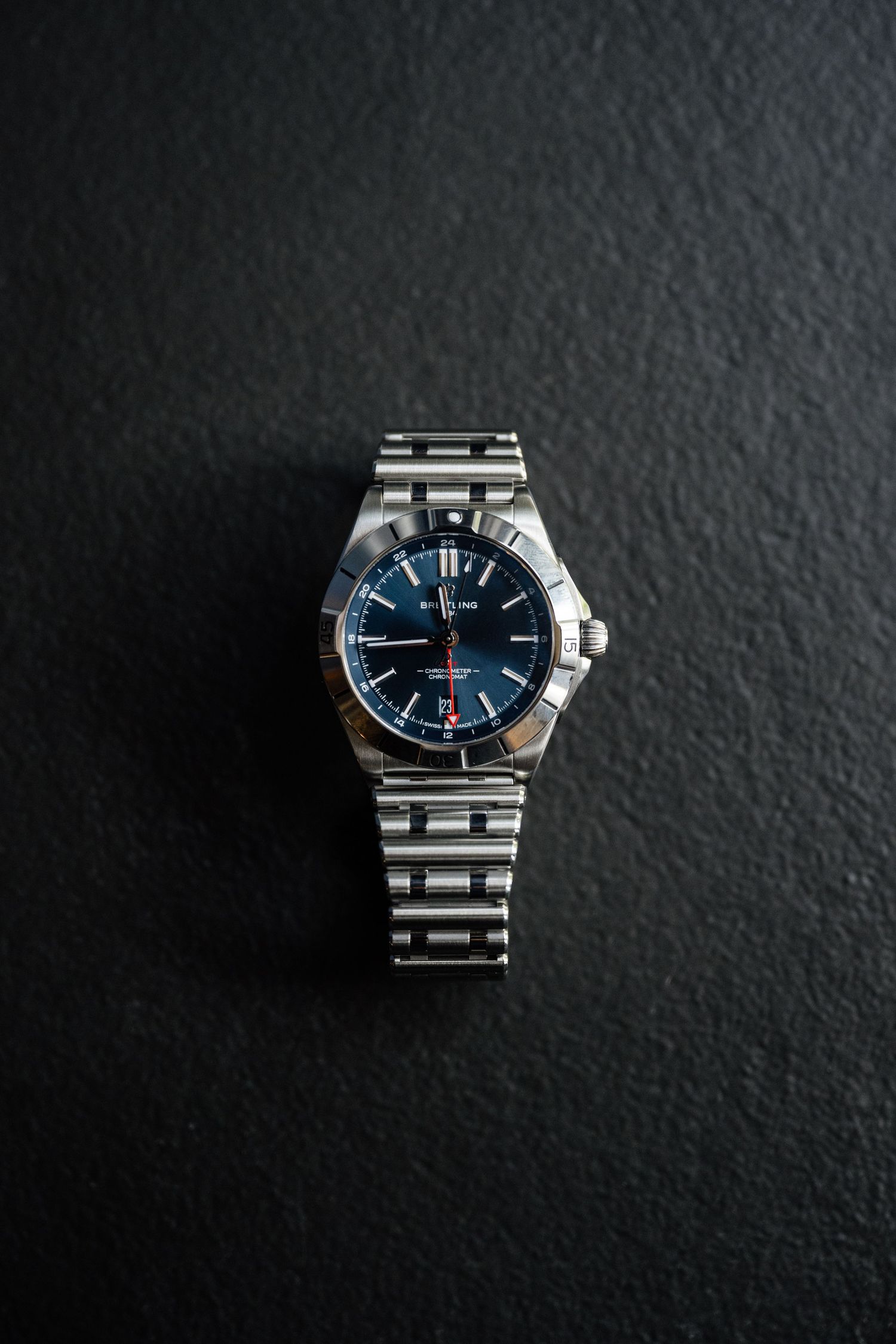 Elegant silver watch with blue face displayed on dark textured surface.