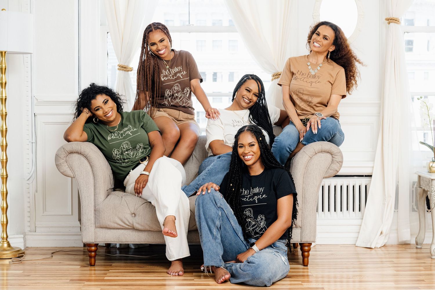 A group of friends lounging together on a light gray couch in a bright white room with hardwood floors.