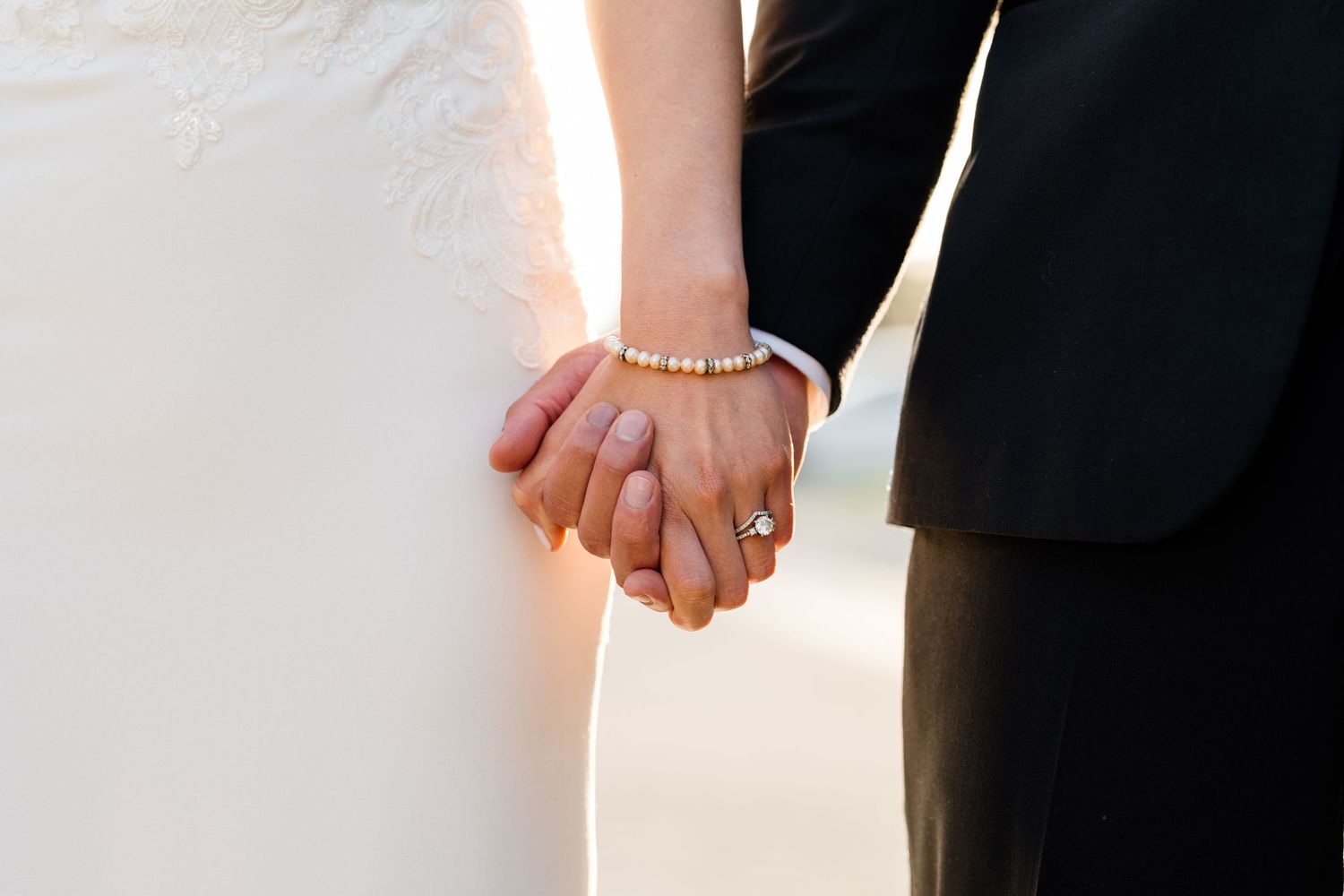 Close-up detail of couple holding hands showing wedding rings and formal attire.