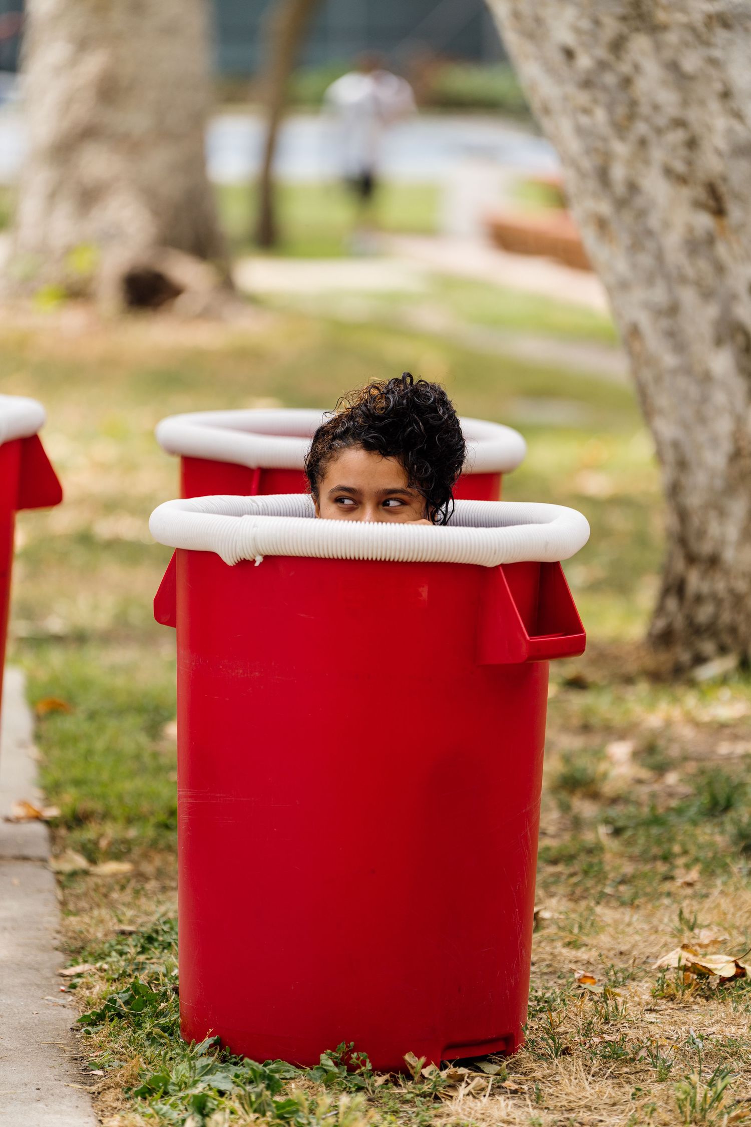 Someone playfully hiding inside a large red container outdoors.