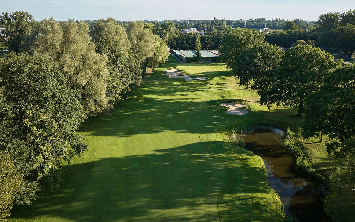 Aerial view of a lush green golf course fairway lined with trees and sand bunkers on a sunny day.