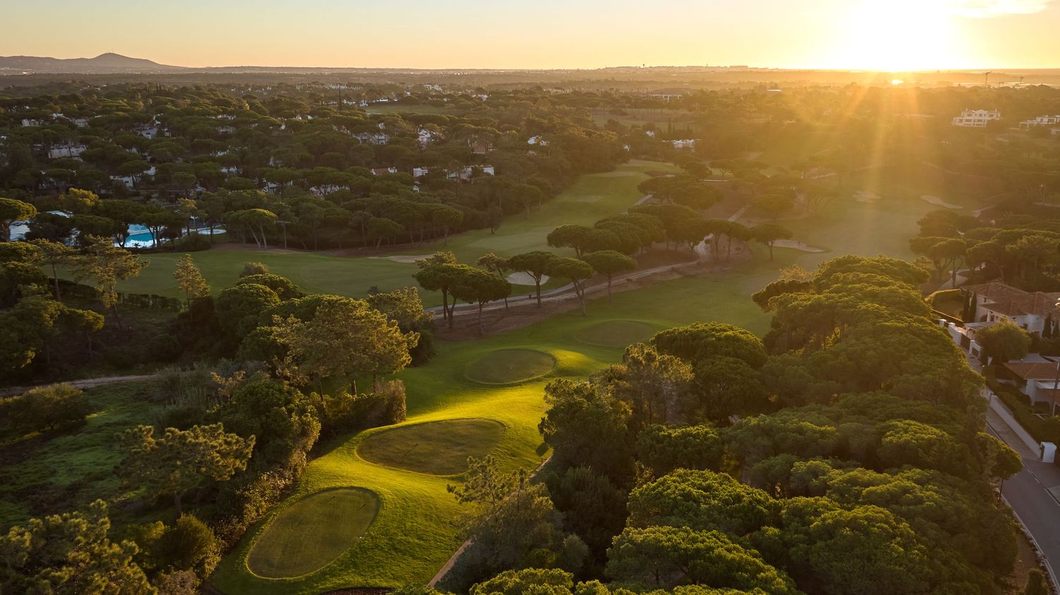 Stunning sunset aerial view of a green golf course with warm golden light rays in the Algarve, Portugal.