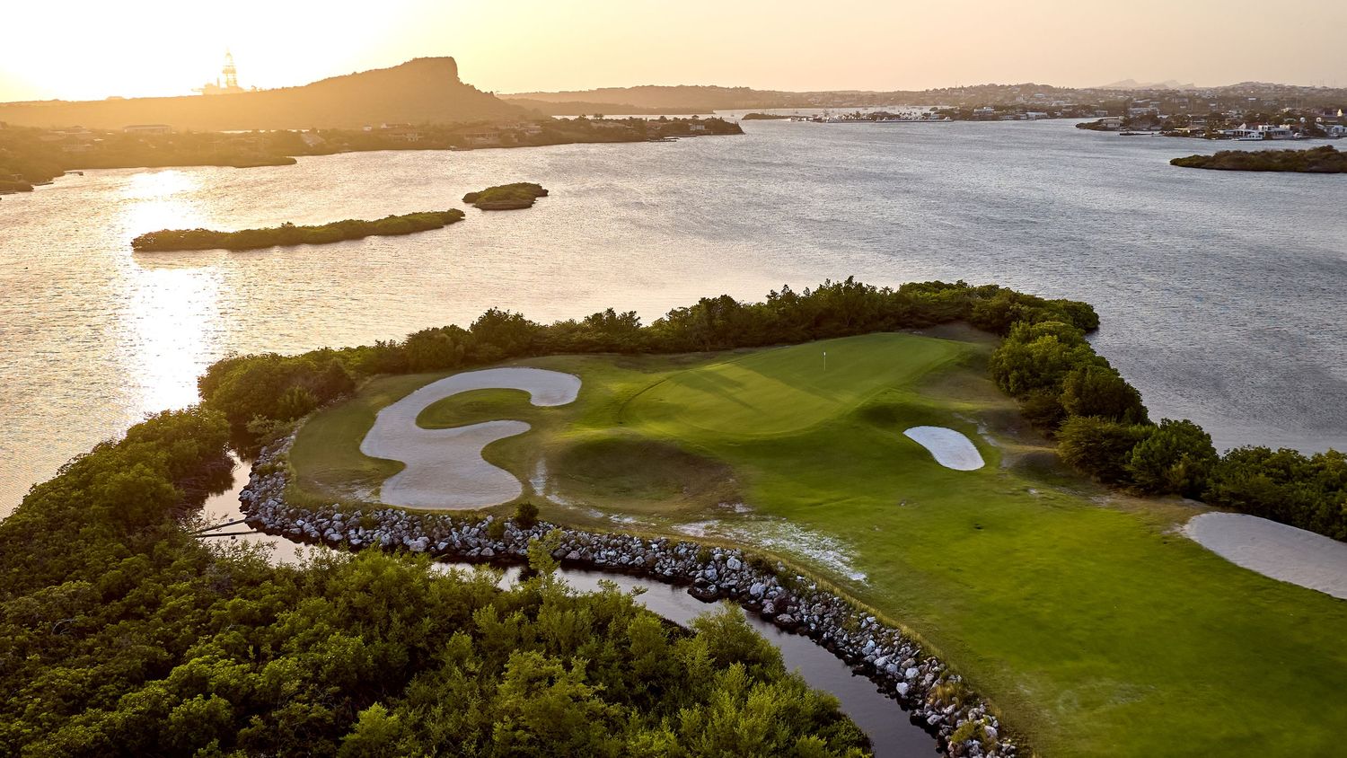 Aerial panoramic view of a coastal golf course with rolling green fairways overlooking the ocean at sunset.