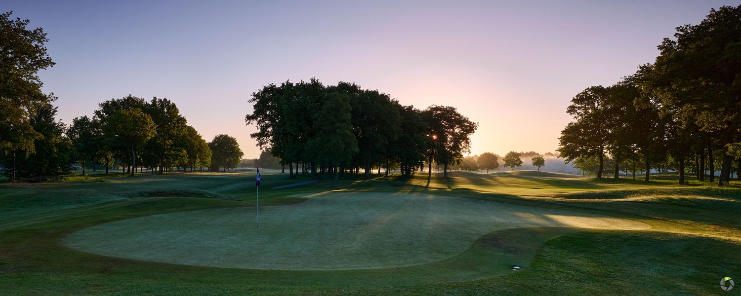 Golden sunrise casting long shadows across a pristine golf course fairway surrounded by mature trees.