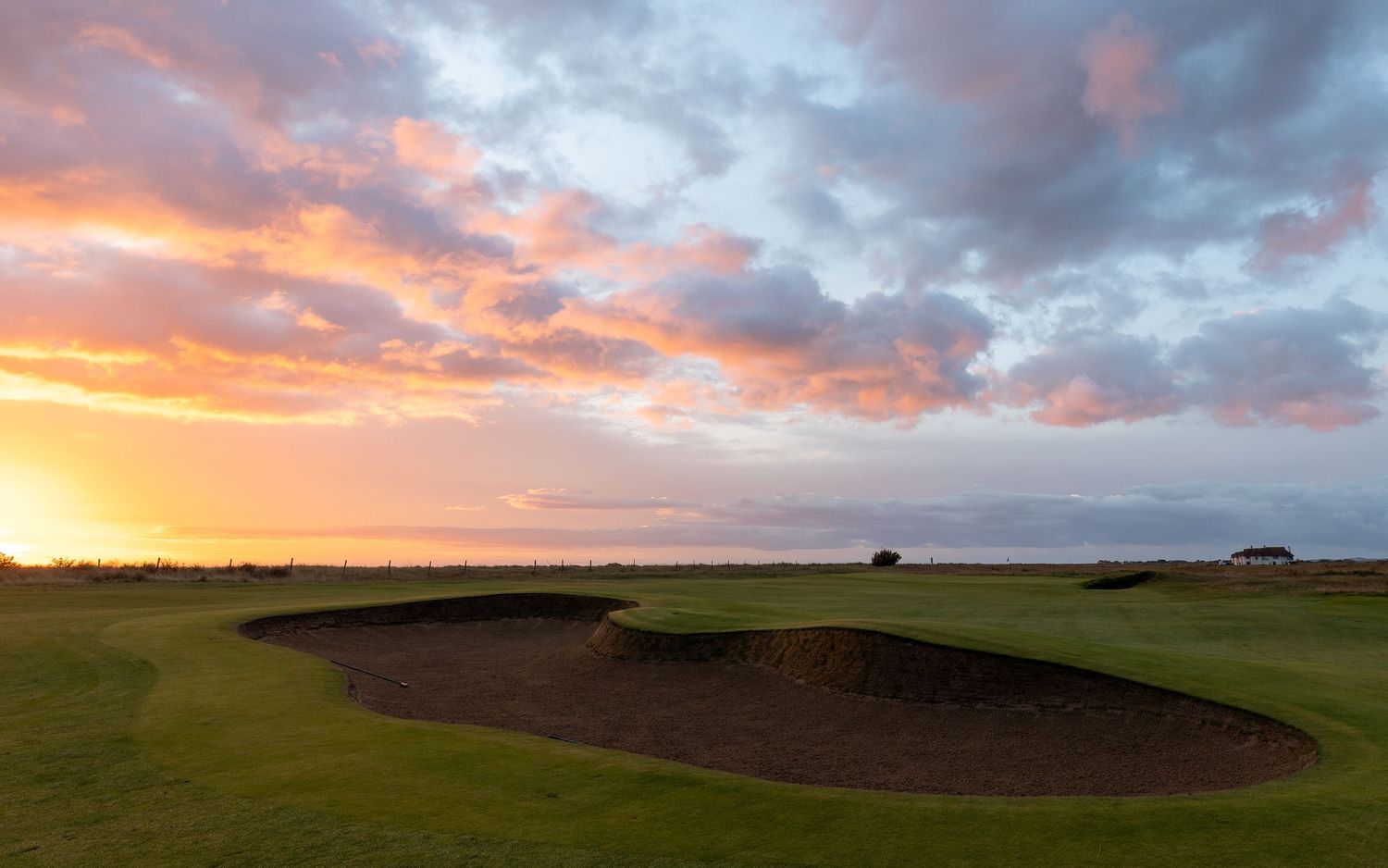 Stunning sunset over a links golf course with sand bunkers and dramatic orange sky reflecting on the green fairways.