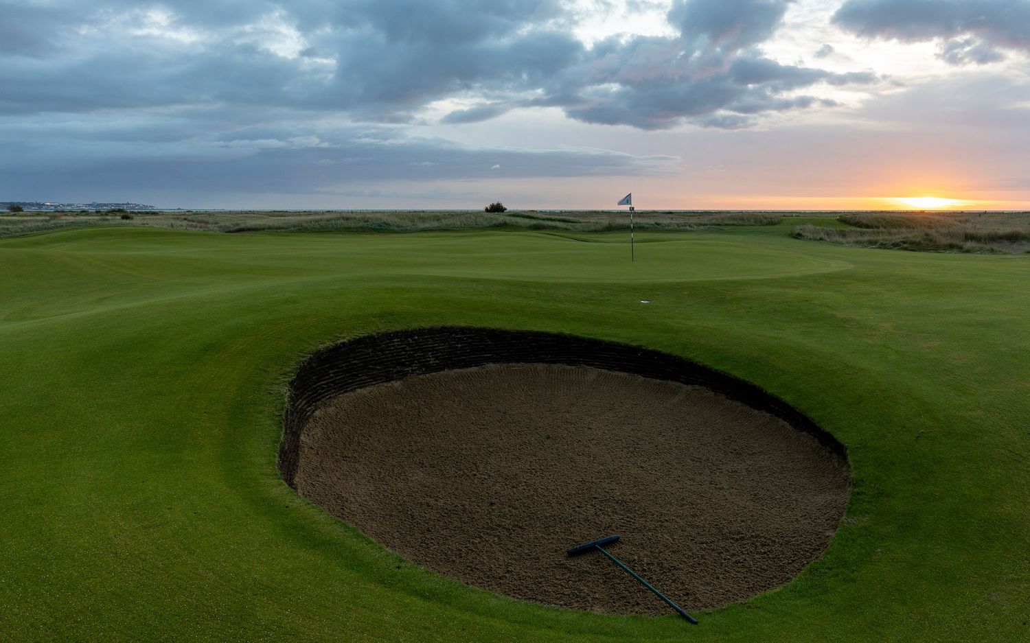 Aerial view of a deep golf course bunker on a links course at sunset with dramatic cloudy skies.