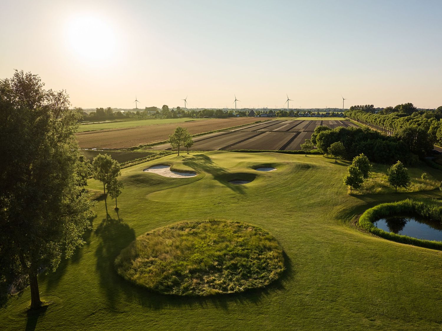 Scenic aerial view of a lush golf course with winding paths, water hazards, and manicured greens in golden sunlight.