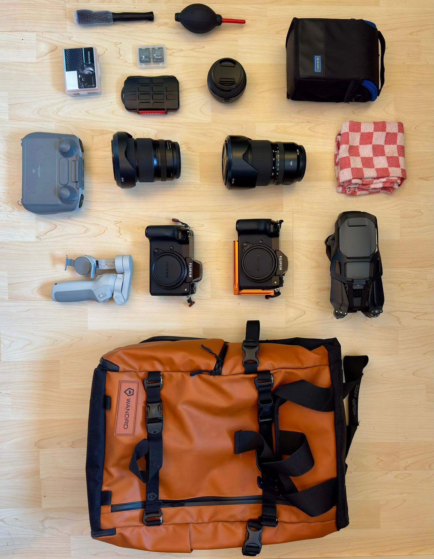 Various camera accessories and bags arranged neatly on a wooden surface including a brown messenger-style camera bag.