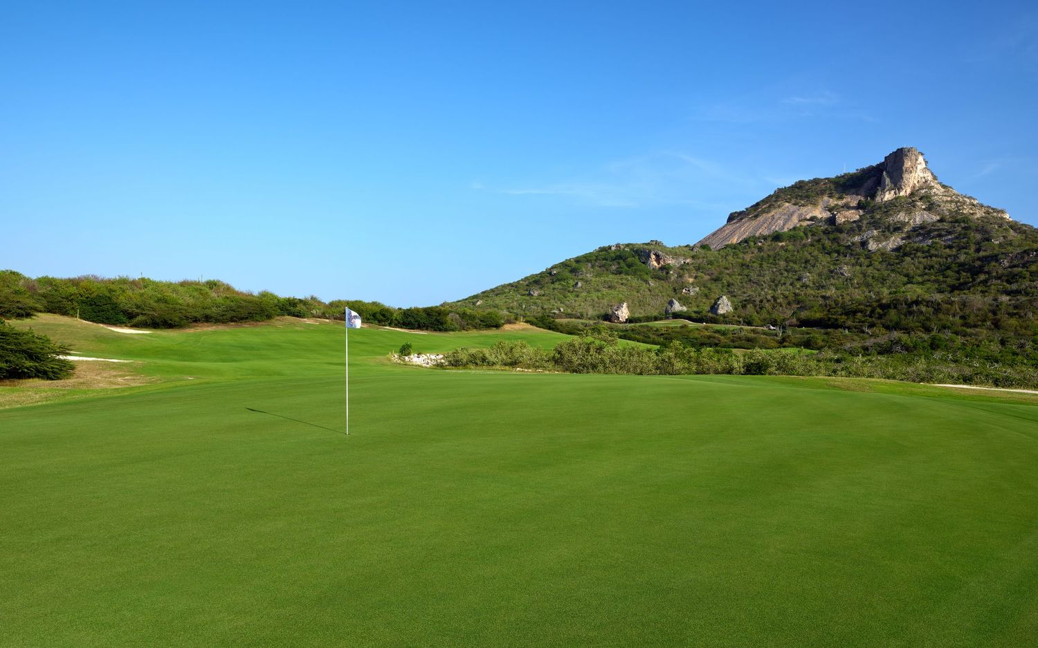 Rolling green fairways and putting greens of a desert golf course with rugged mountains in the background.