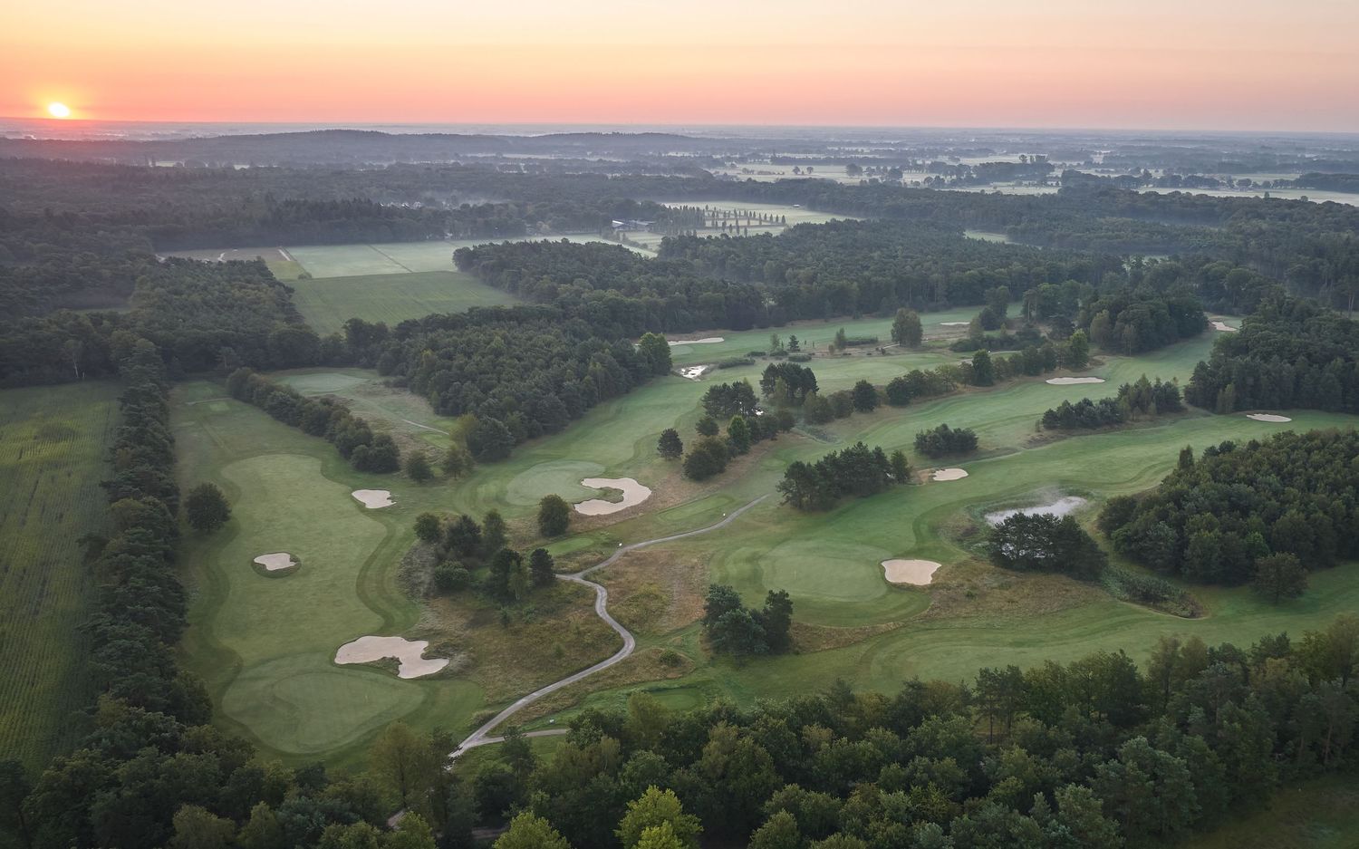 Panoramic aerial view of rolling green hills with scattered barns and farmland at sunset.