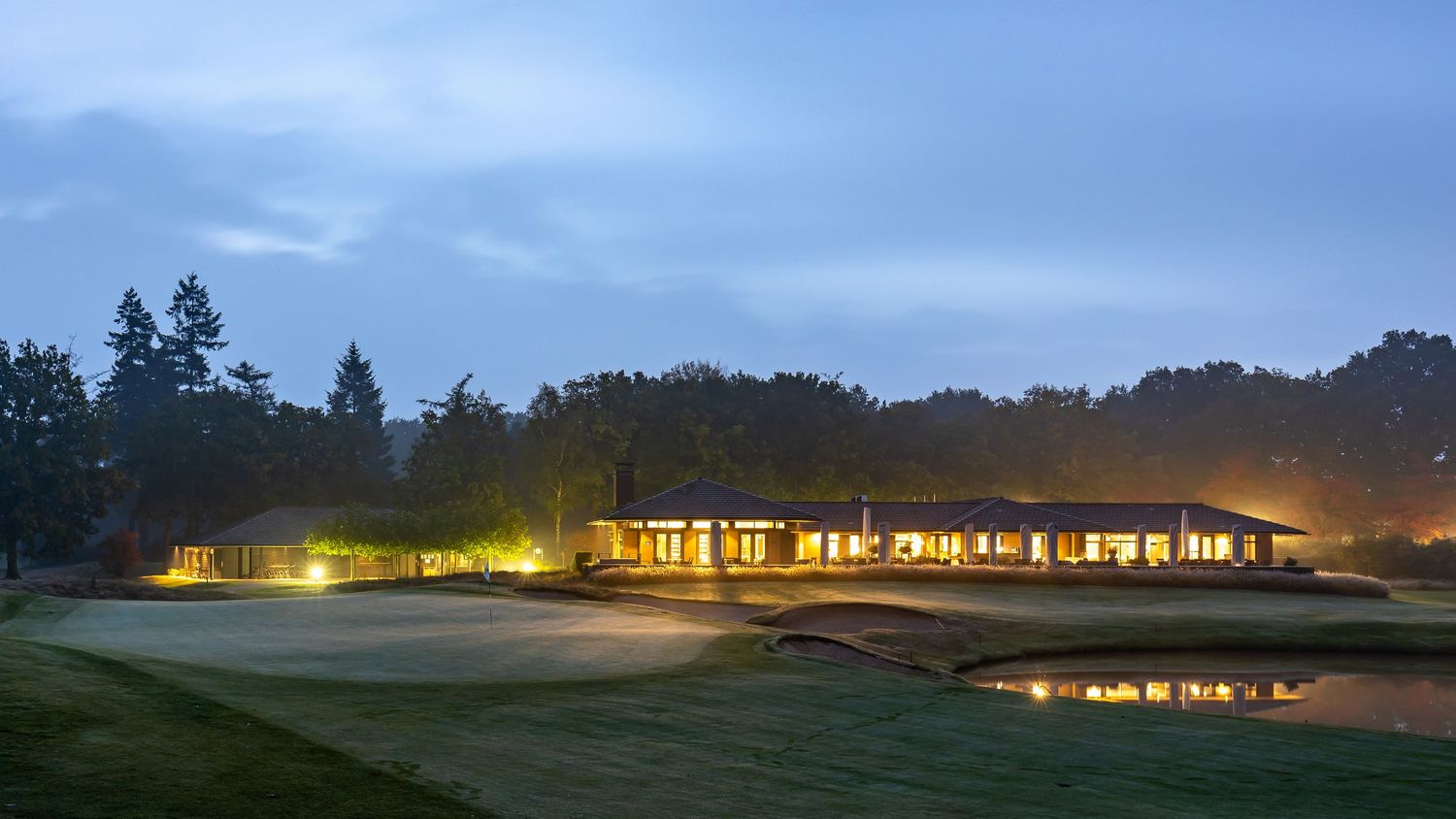 A panoramic twilight view of illuminated buildings and trees stretching across a serene rural landscape.