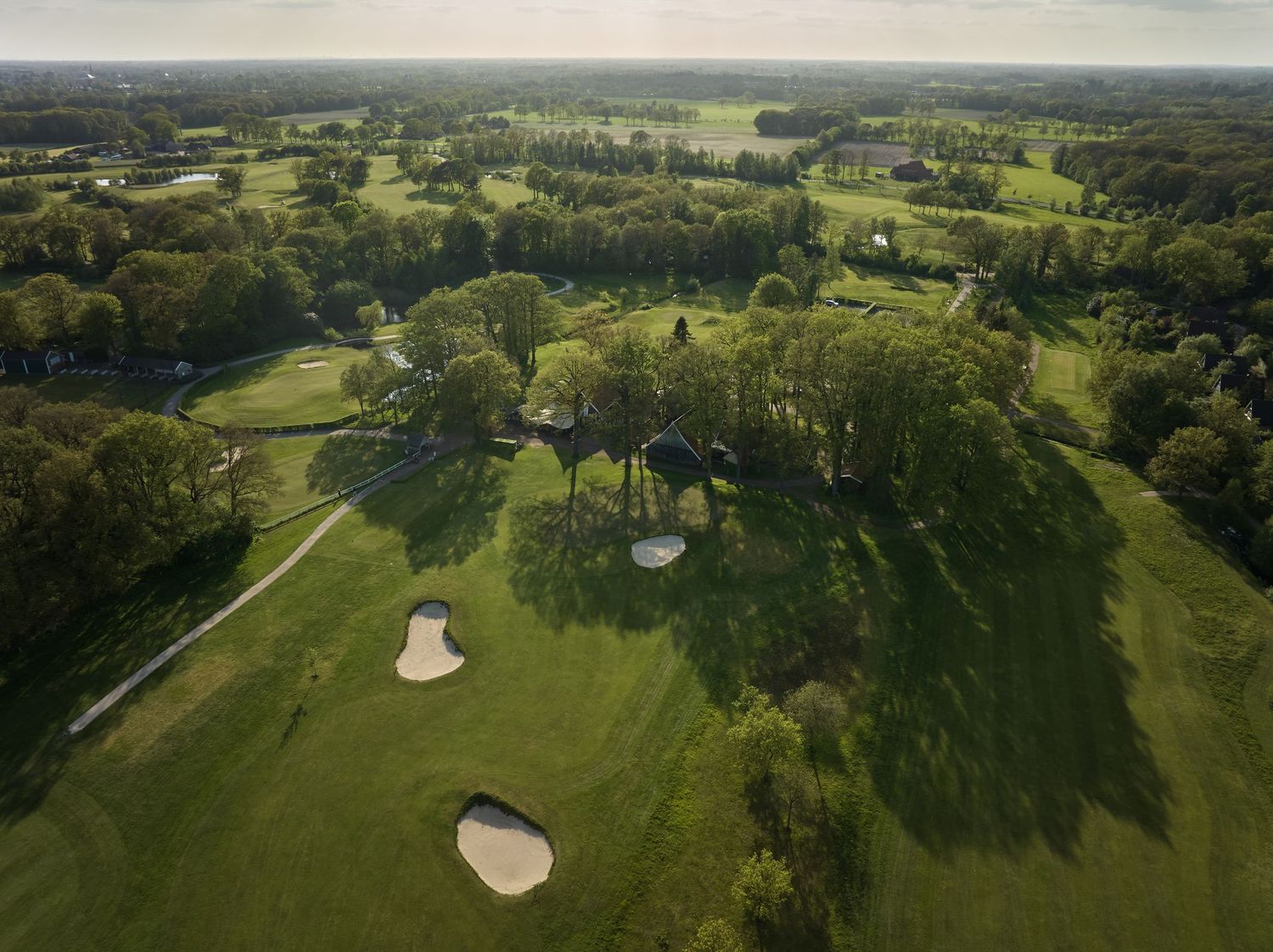 Aerial view of a lush green golf course with sand bunkers and winding fairways surrounded by trees and countryside.