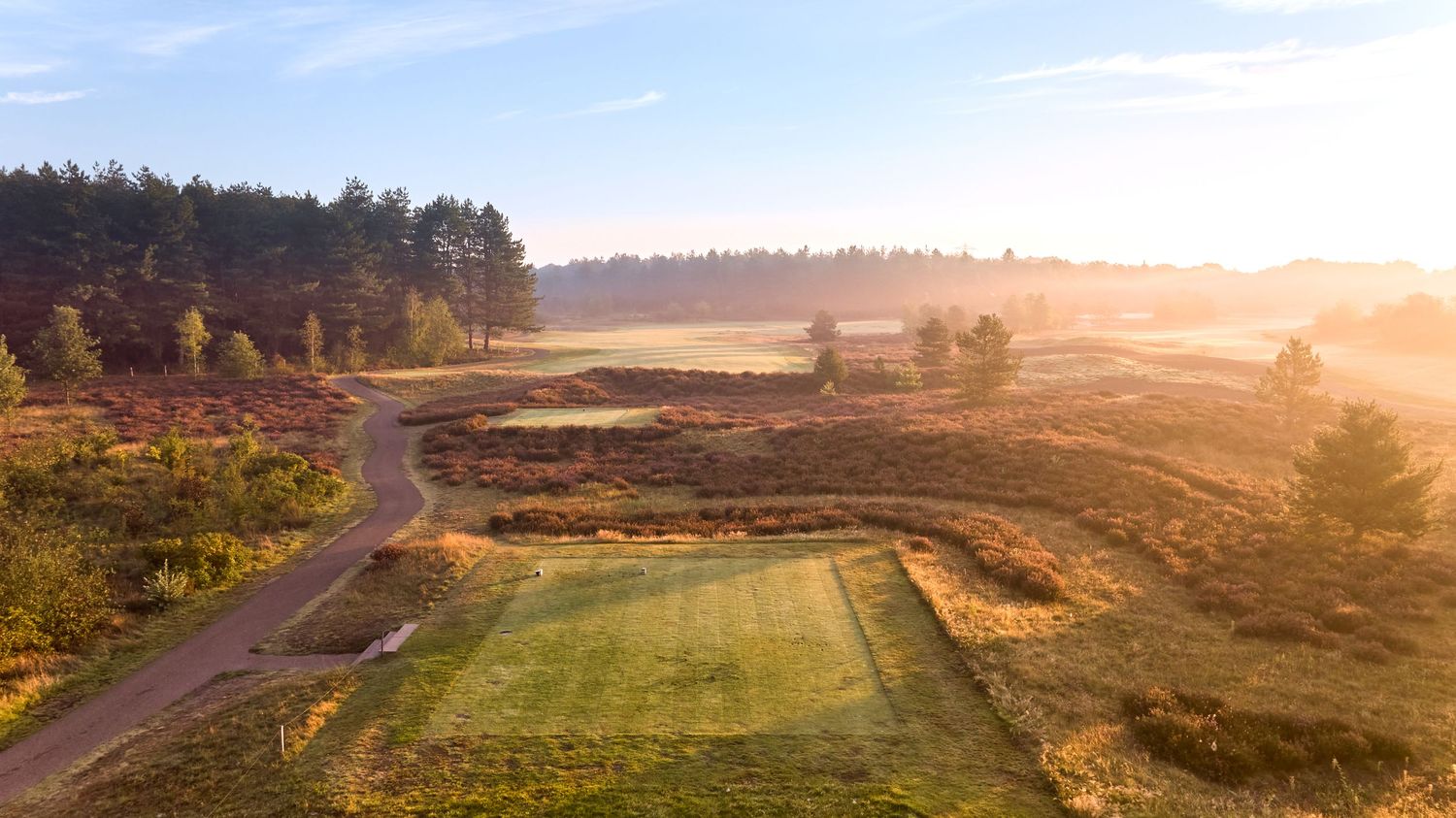 Aerial view of a misty golf course fairway at sunrise with heathland surroundings.
