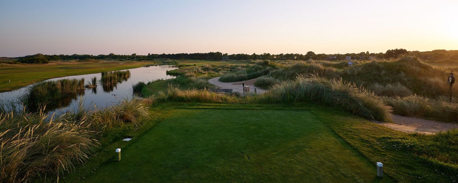 Aerial view of a scenic golf course fairway with winding water hazards and lush grass at sunset.
